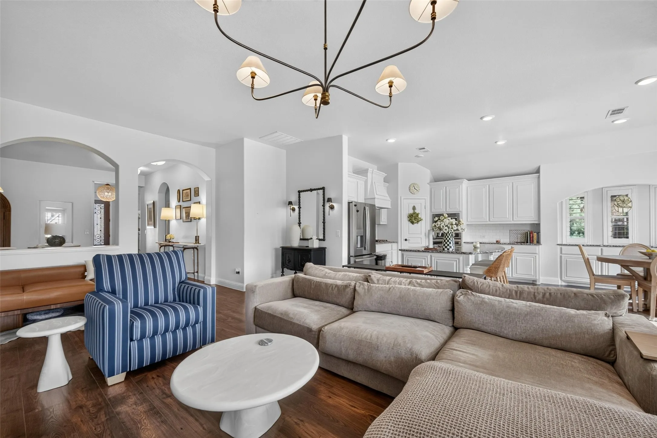 Open-concept interior featuring wood-finish flooring, architectural archways, a multi-arm chandelier, recessed lighting, and kitchen cabinetry with a central island