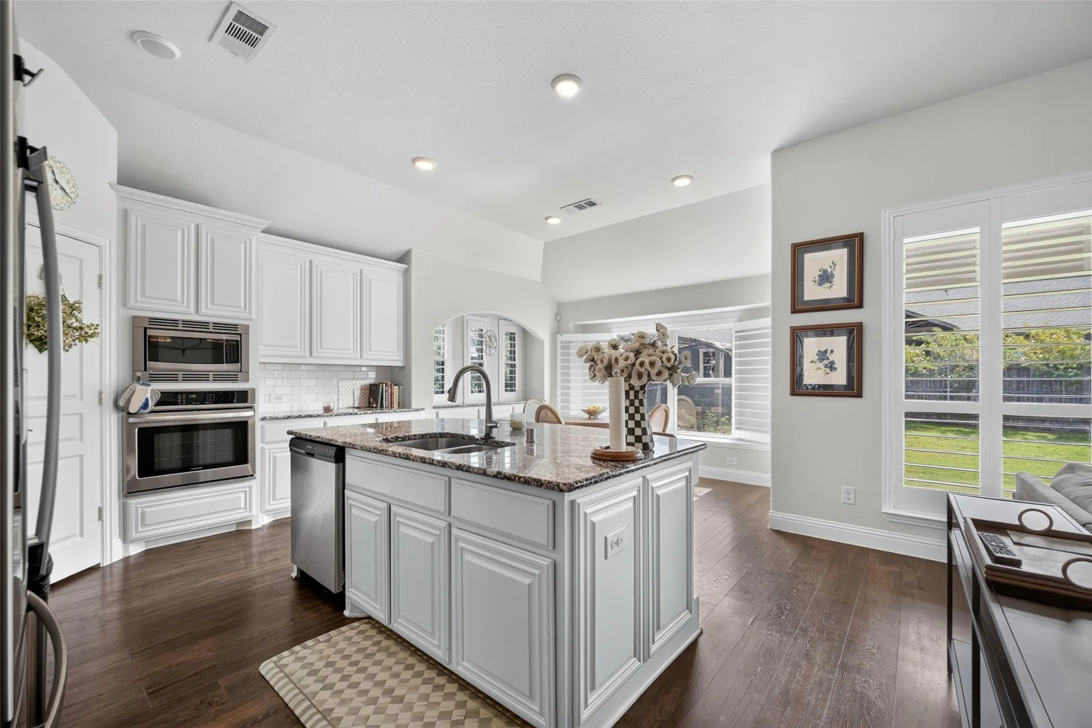 Kitchen featuring white cabinetry, stone-surface island with an undermount sink, built-in wall oven and microwave, and wood-finish flooring