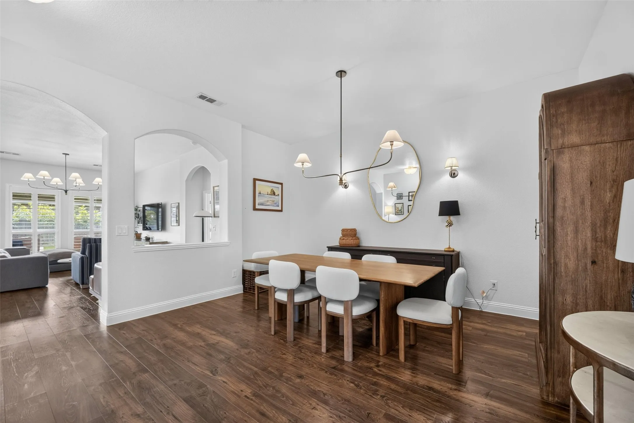 Dining area featuring wood-finish flooring, an arched wall cutout, a contemporary multi-arm chandelier, and wall-mounted lighting