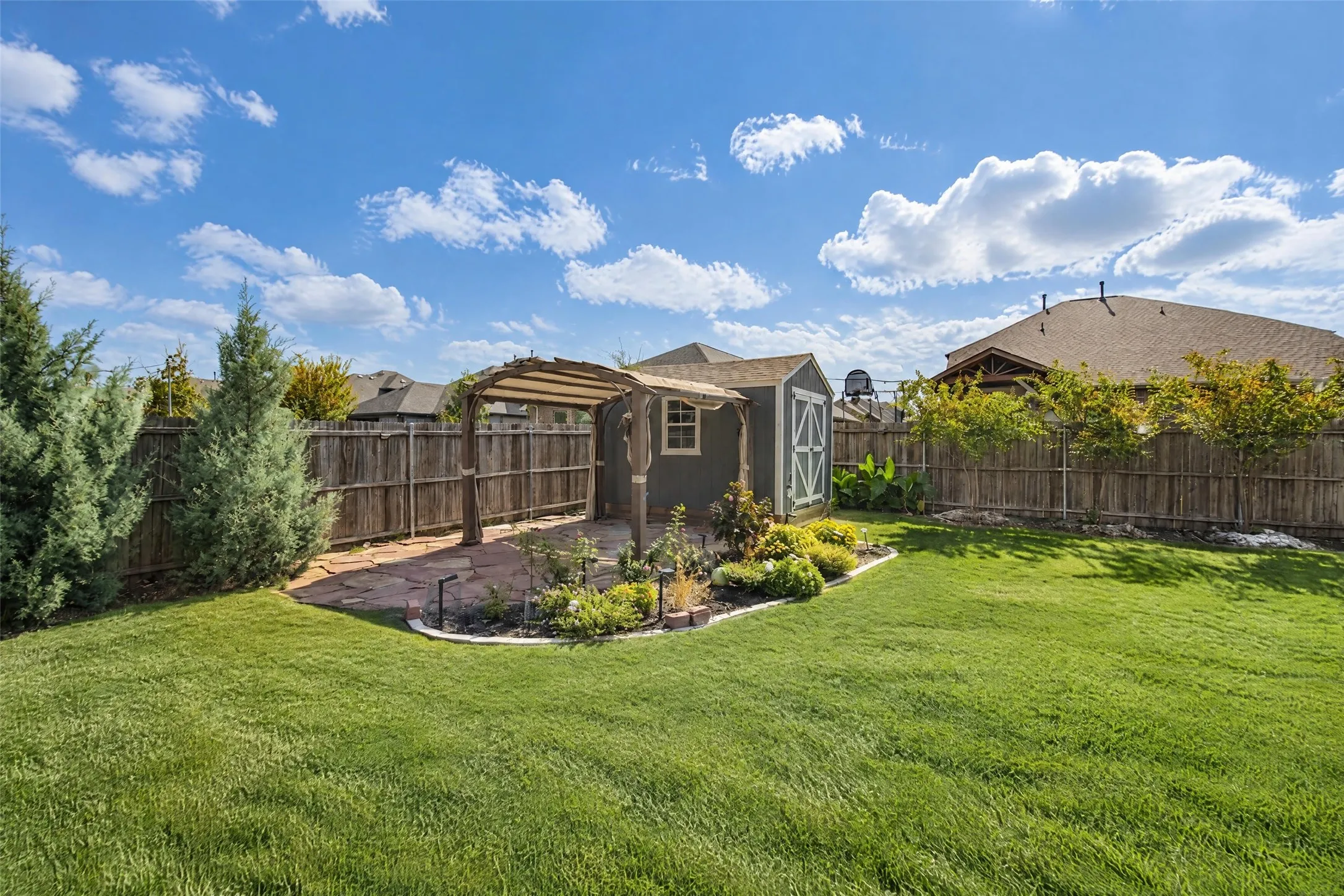 Backyard featuring a manicured lawn, stone-paver patio, wood-frame pergola, storage structure, and perimeter wood privacy fencing