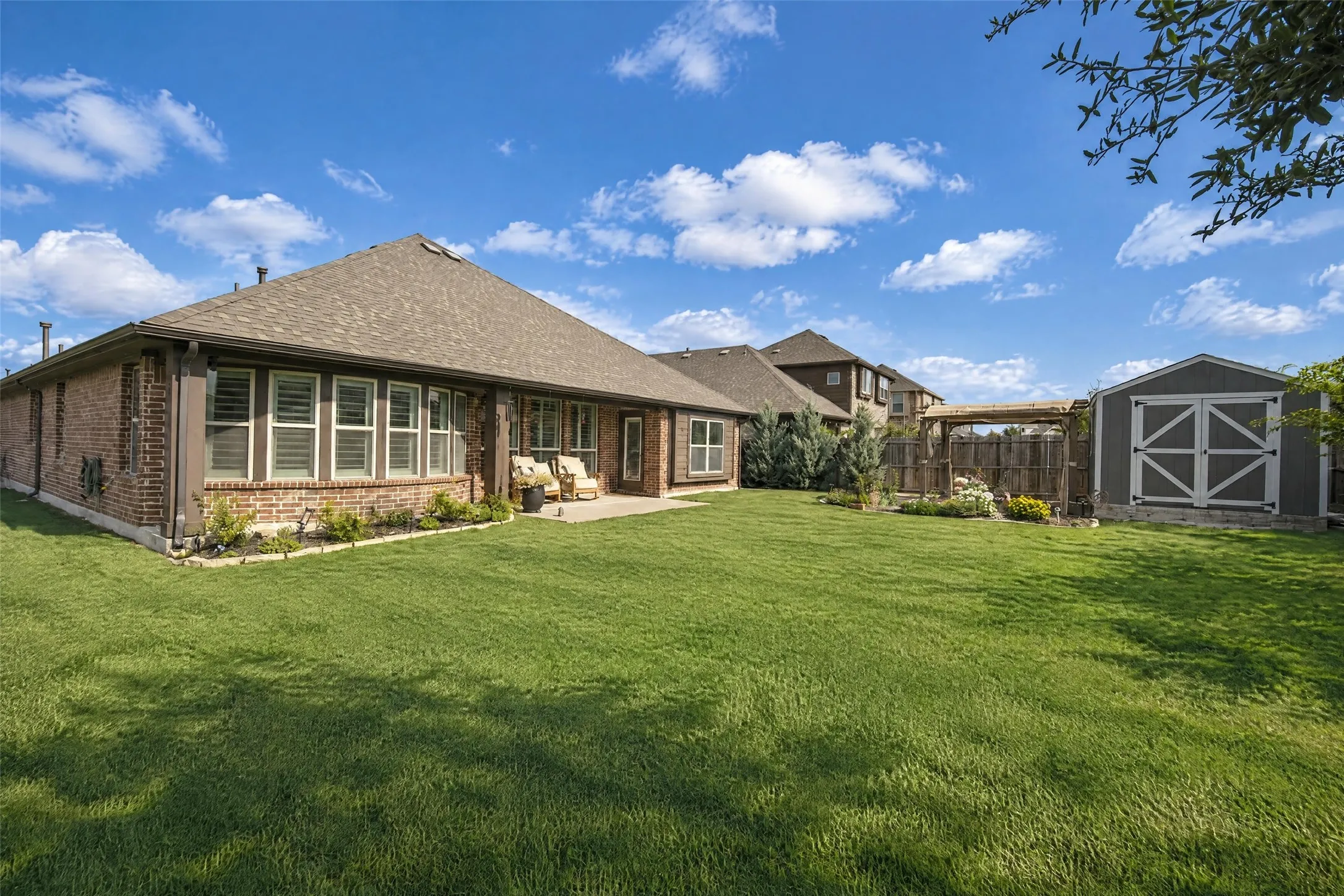 Backyard featuring a brick-exterior residence, a concrete patio, a wood-framed pergola, and a detached storage structure