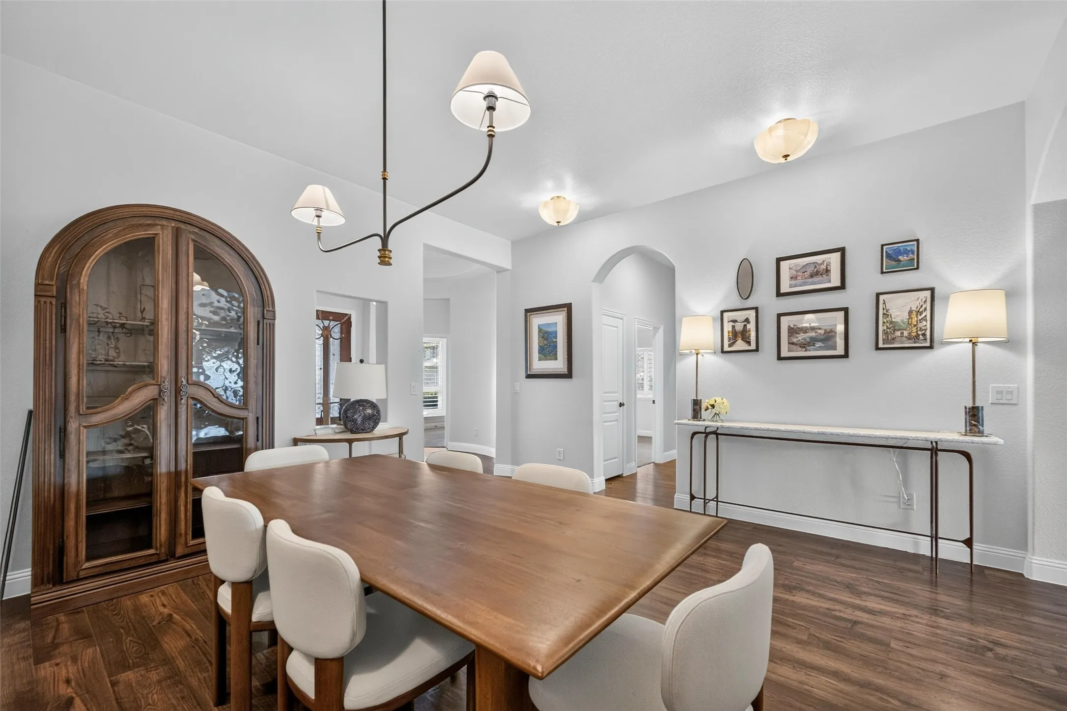 Dining area featuring wood-finish flooring, an arched doorway, and a built-in arched wooden display cabinet with glass shelving