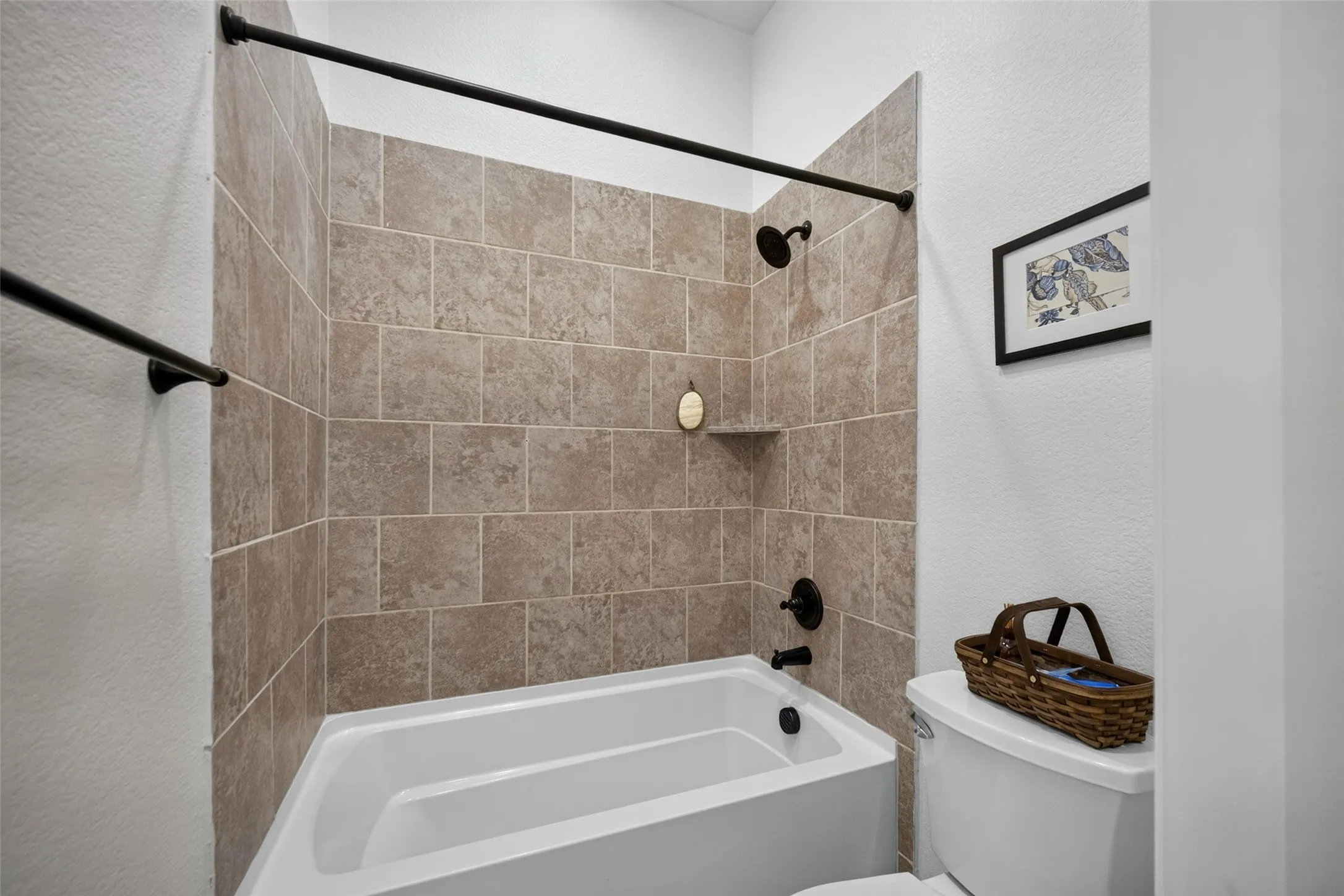Bathtub enclosure featuring neutral-toned tiled surround, matte black shower head, matching faucet fixture, and integrated soap niche