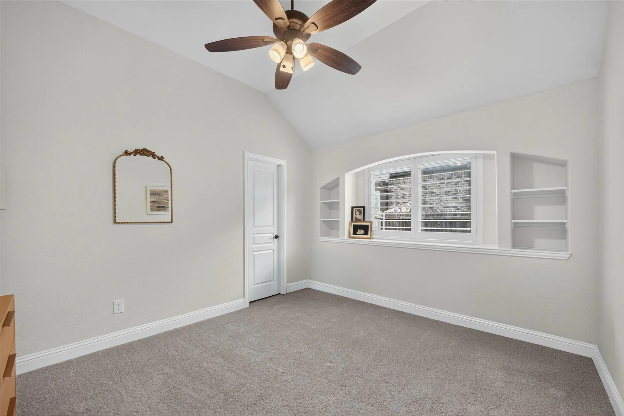 Vaulted ceilings, built-in shelving, arched window recess with shutter treatments, and a central ceiling fan with multi-light fixture