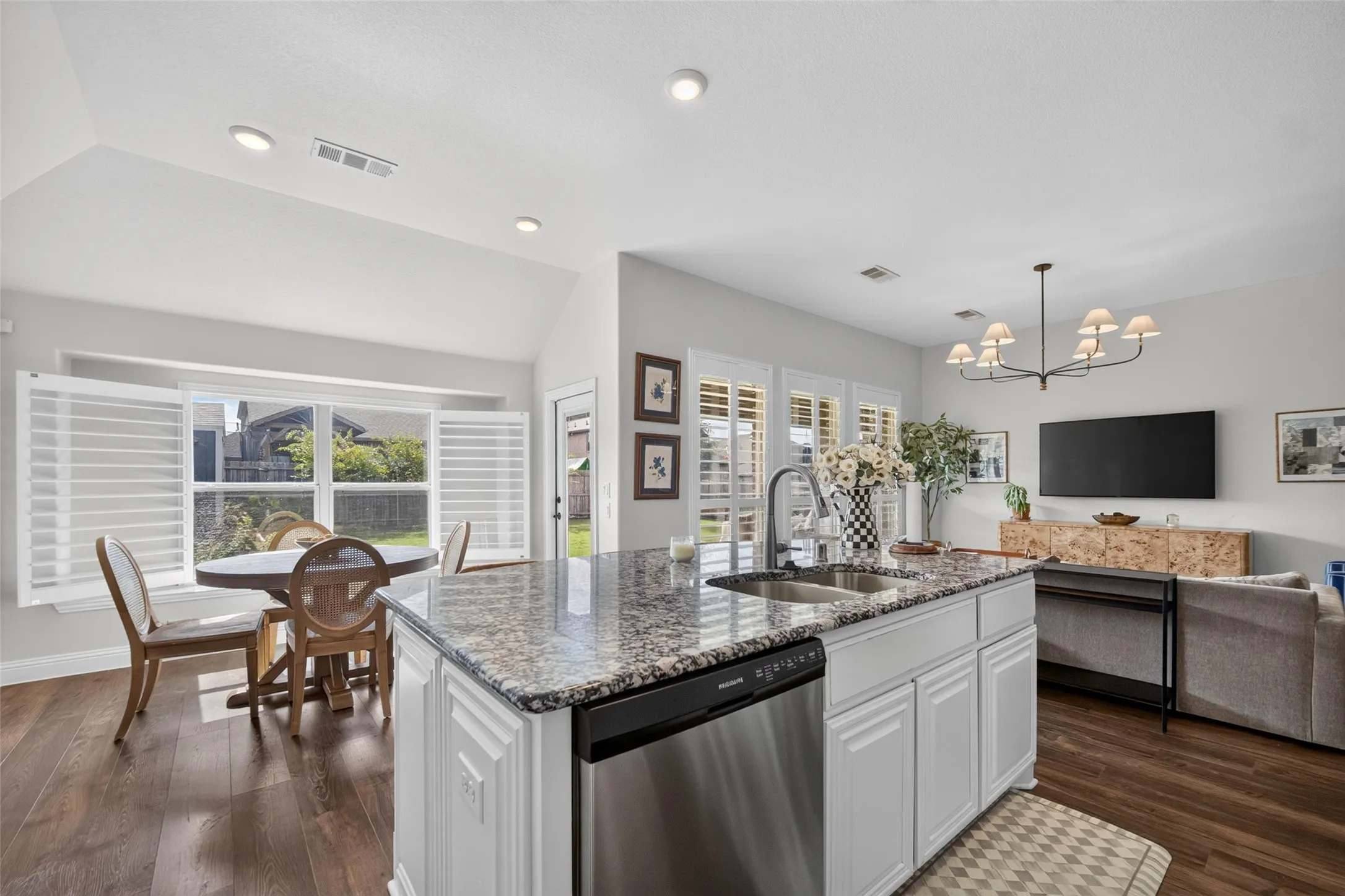 Kitchen island featuring a stone-look countertop, undermount sink, and stainless steel dishwasher, vaulted ceilings, wood-finish flooring, and white plantation shutters
