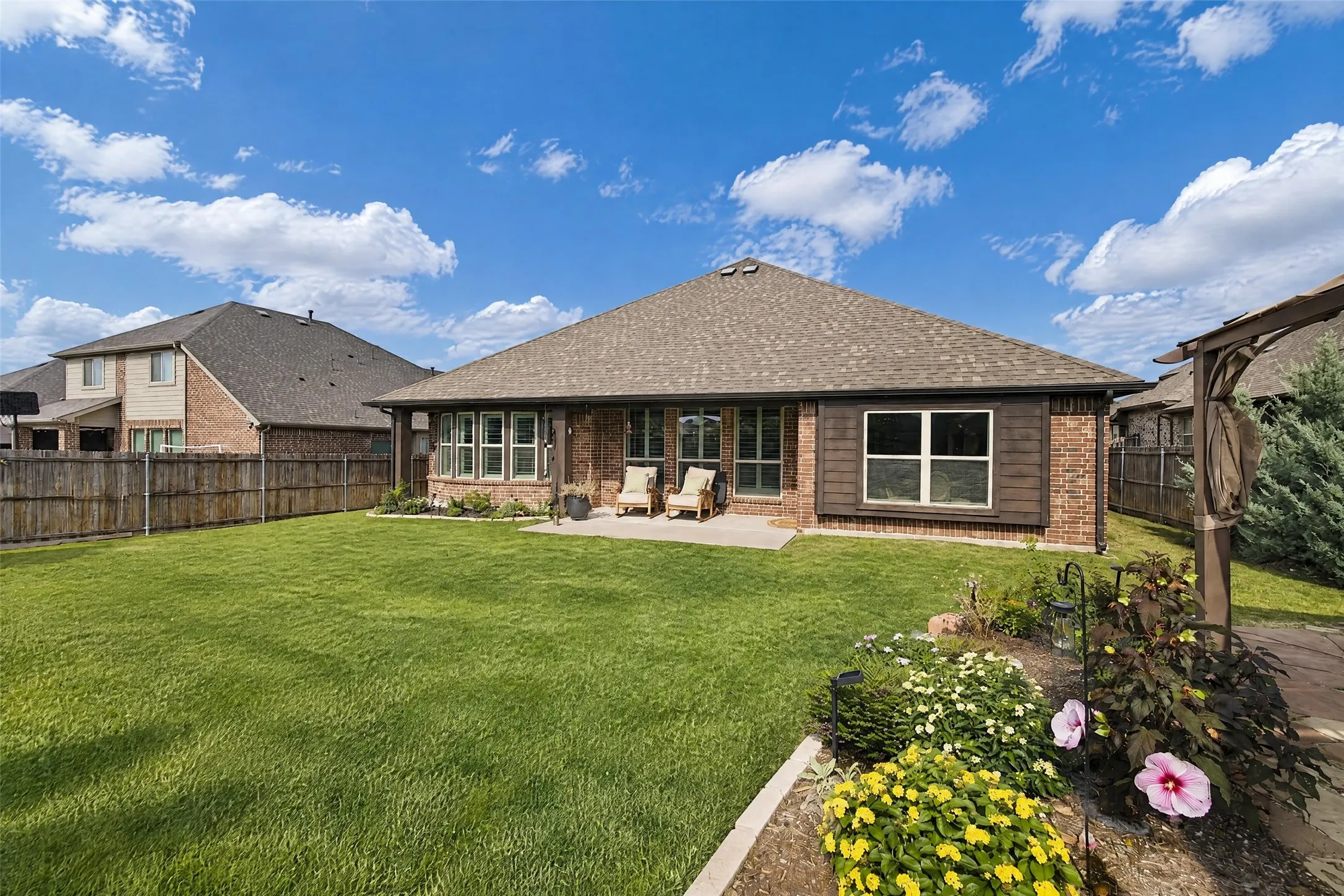 Brick exterior featuring a concrete patio, wood-style trim accents, and a fenced backyard with landscaped garden beds