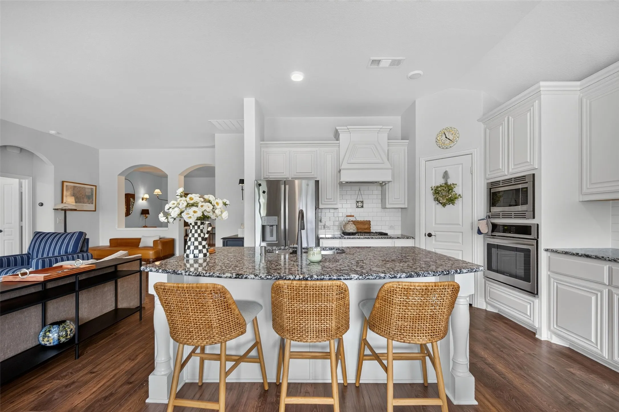 Kitchen featuring white cabinetry, stone-surfaced center island with seating area, stainless steel built-in wall oven and microwave, subway tile backsplash, and wood-finish flooring