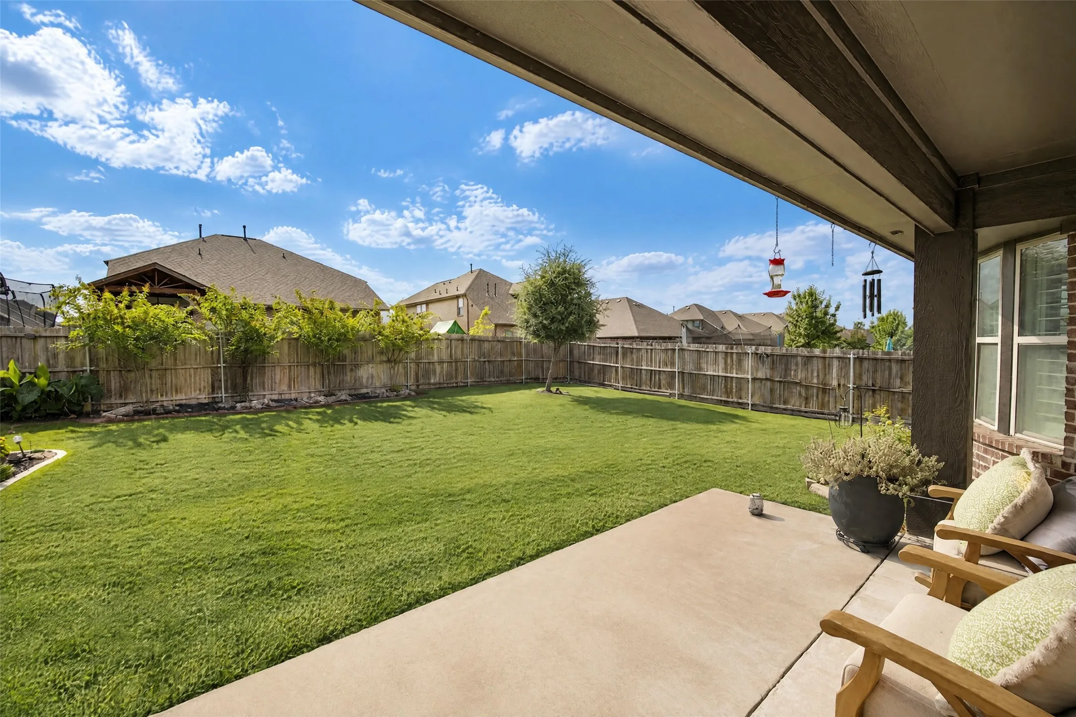 Covered concrete patio overlooking a private backyard featuring a manicured lawn, wooden perimeter fencing, and mature landscaping