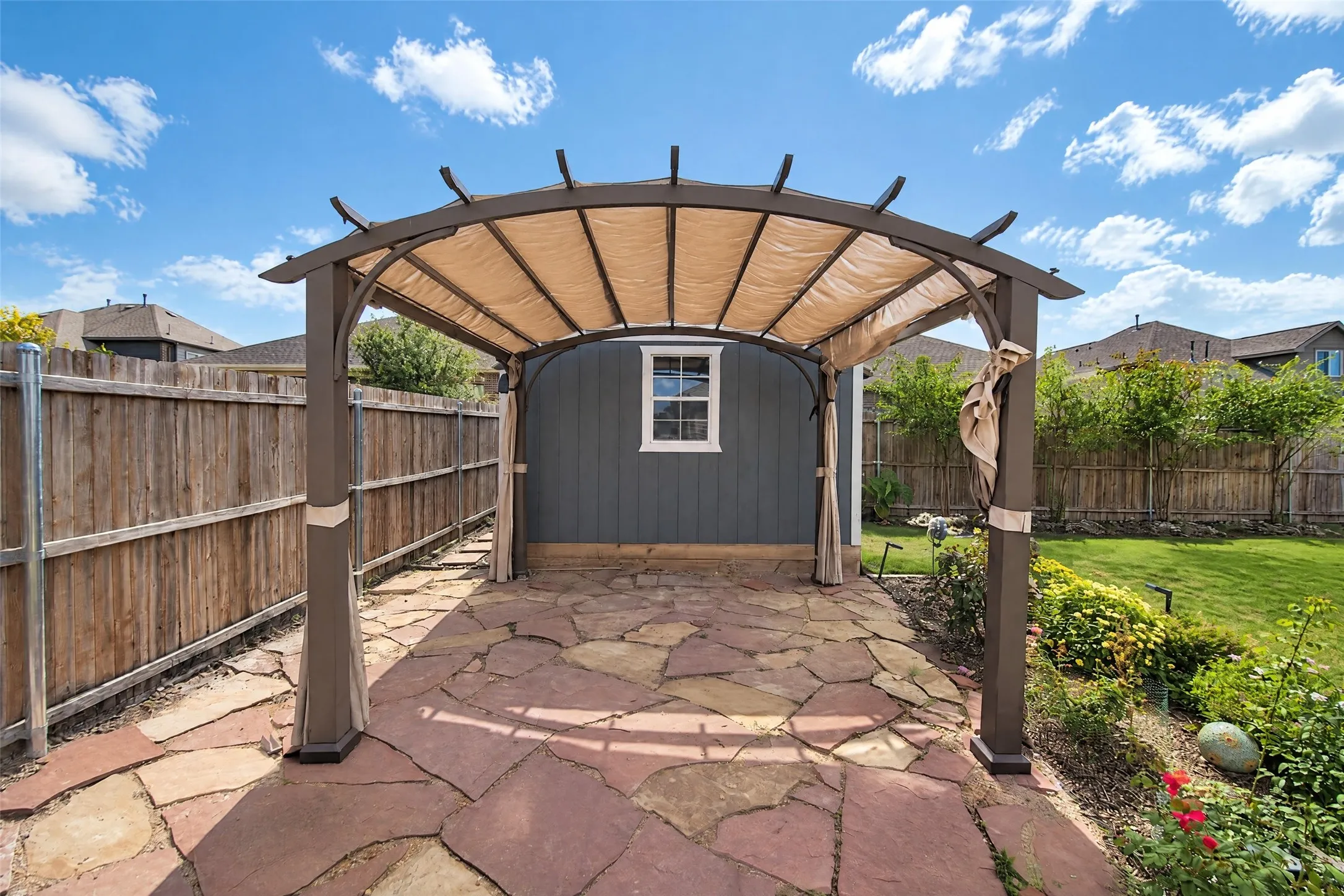 Backyard space featuring a flagstone patio, metal-frame pergola with fabric canopy, and wood-paneled exterior siding