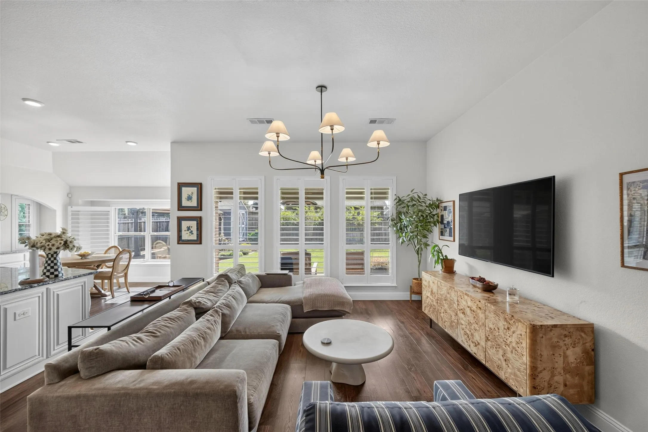 Open-concept living space featuring wood-finish flooring, a multi-arm chandelier, and three sets of plantation shutters