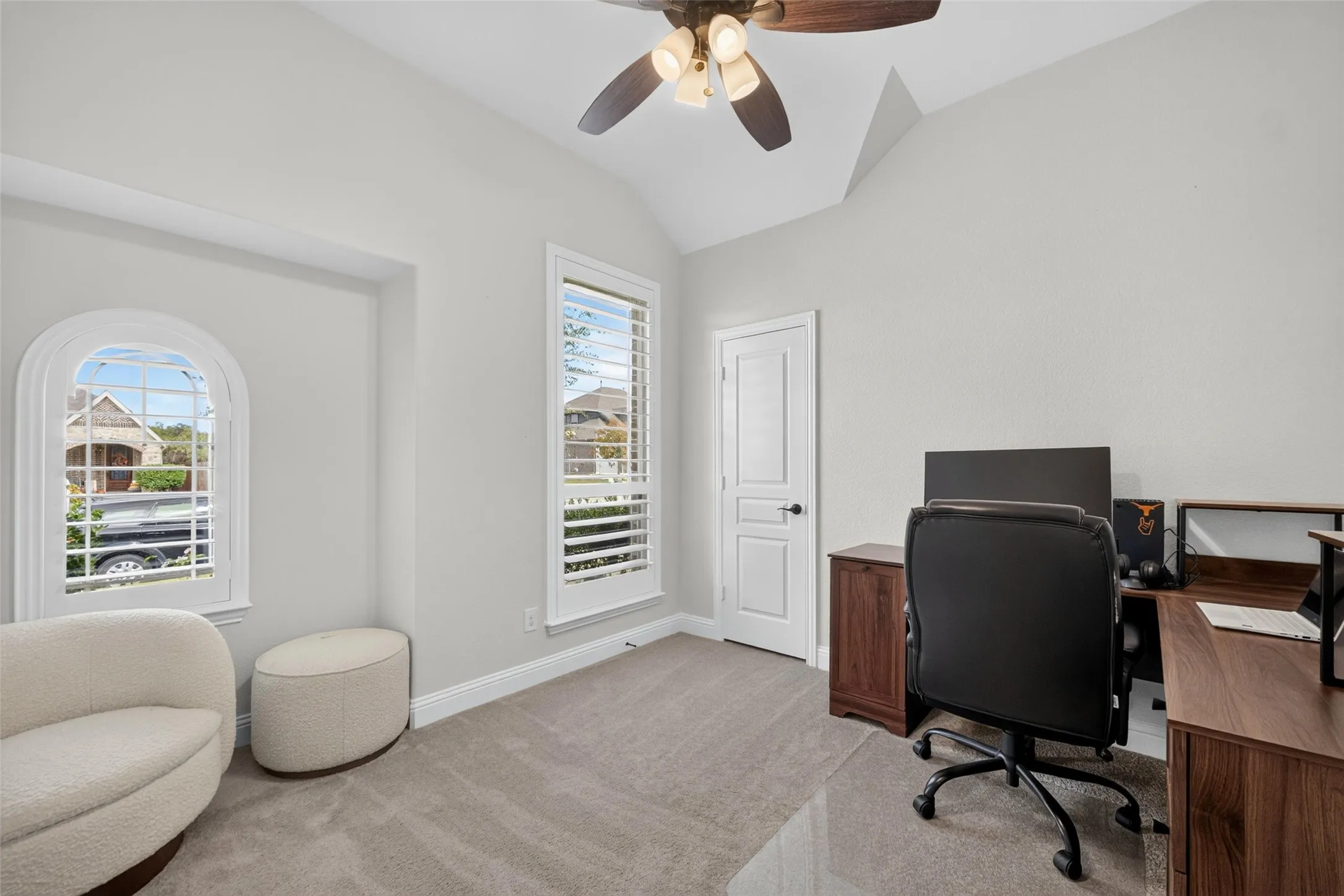 Vaulted ceilings, arched window, plantation shutters, neutral carpeting, and a ceiling fan with integrated lighting