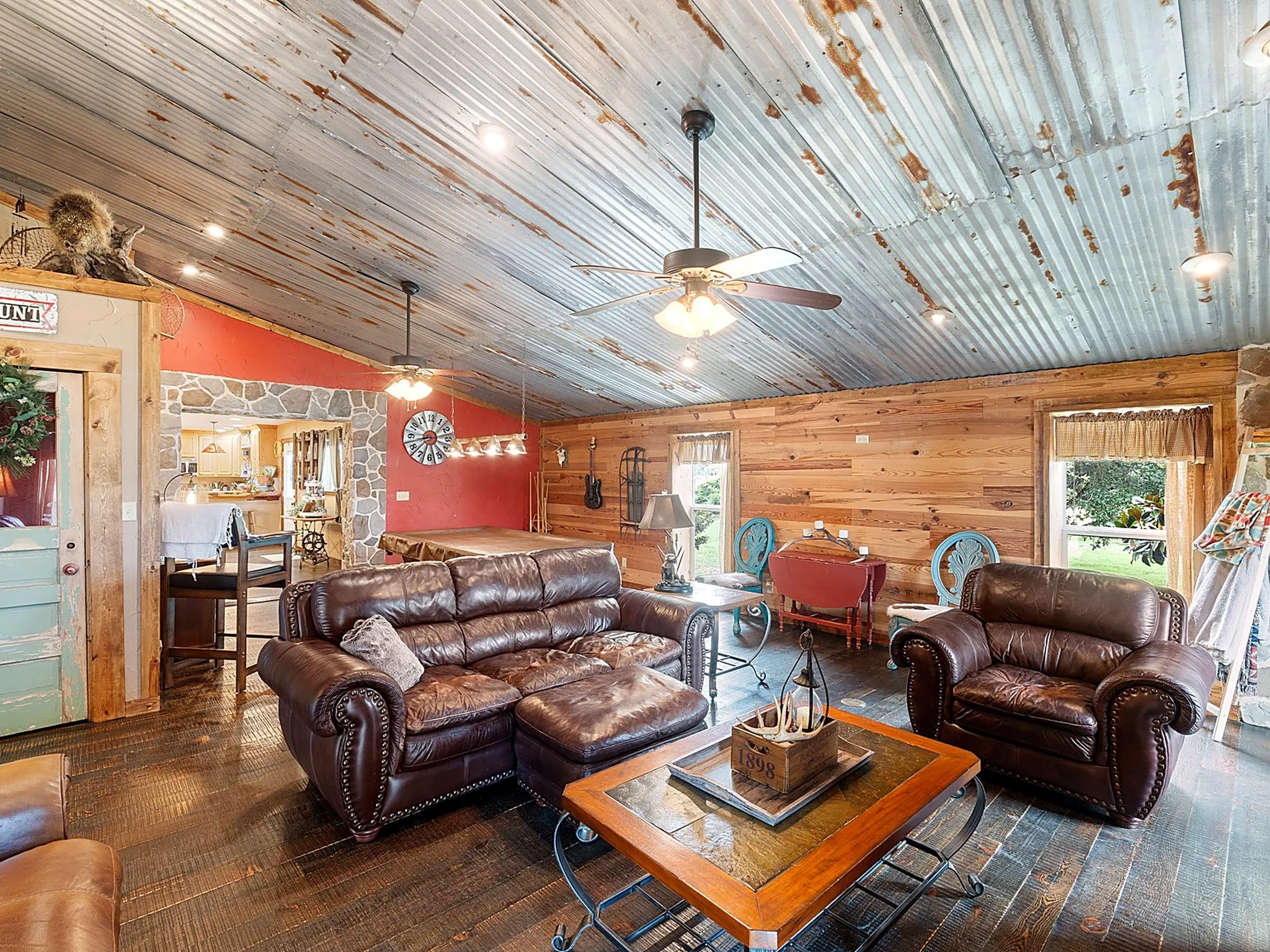 Vaulted ceiling with corrugated metal cladding, horizontal wood-plank wall paneling, natural stone accents, dark wood-finish flooring, and integrated ceiling fans