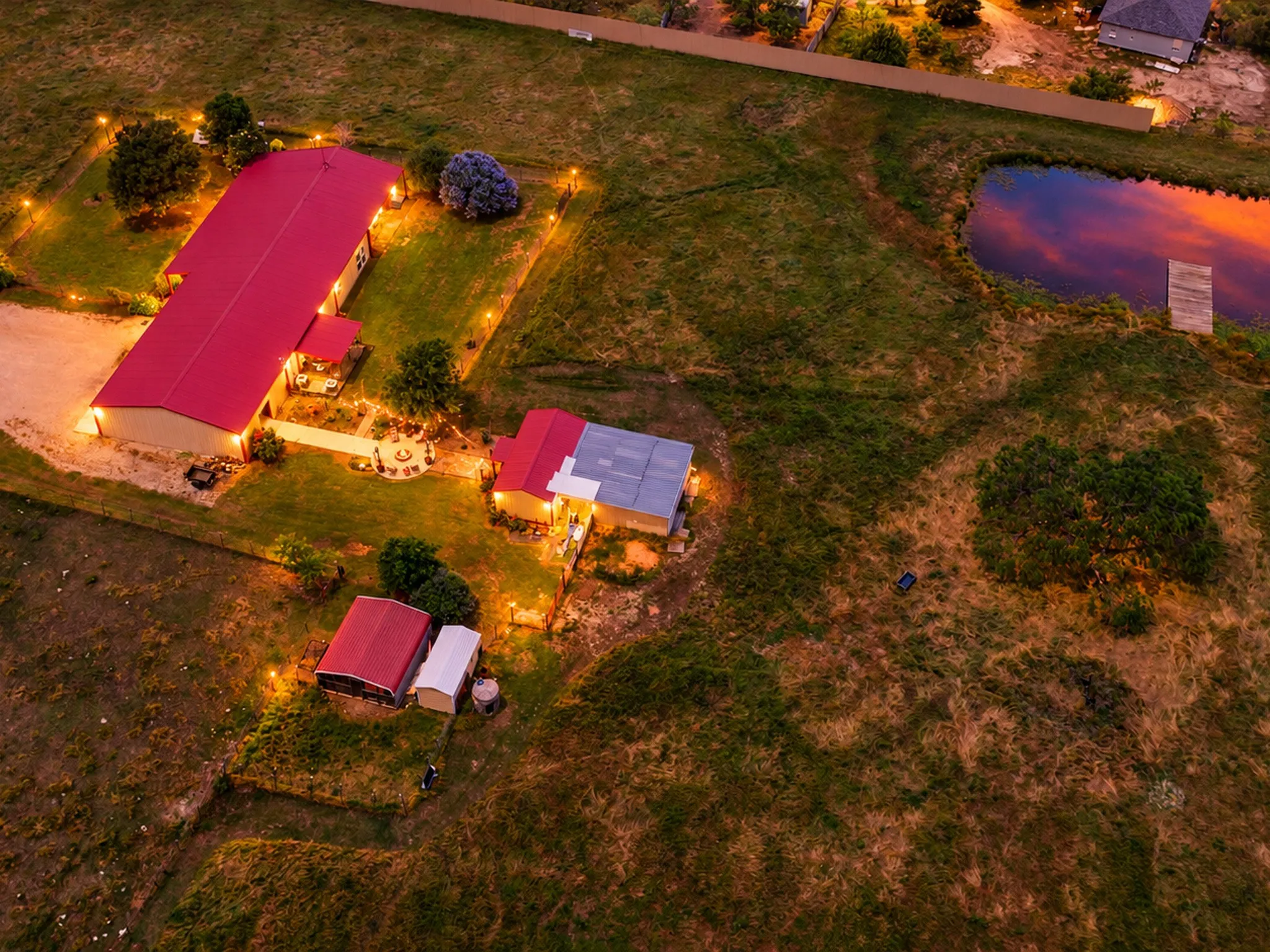 Expansive property featuring multiple structures with red metal roofs, a private pond with a wooden dock, and extensive grounds