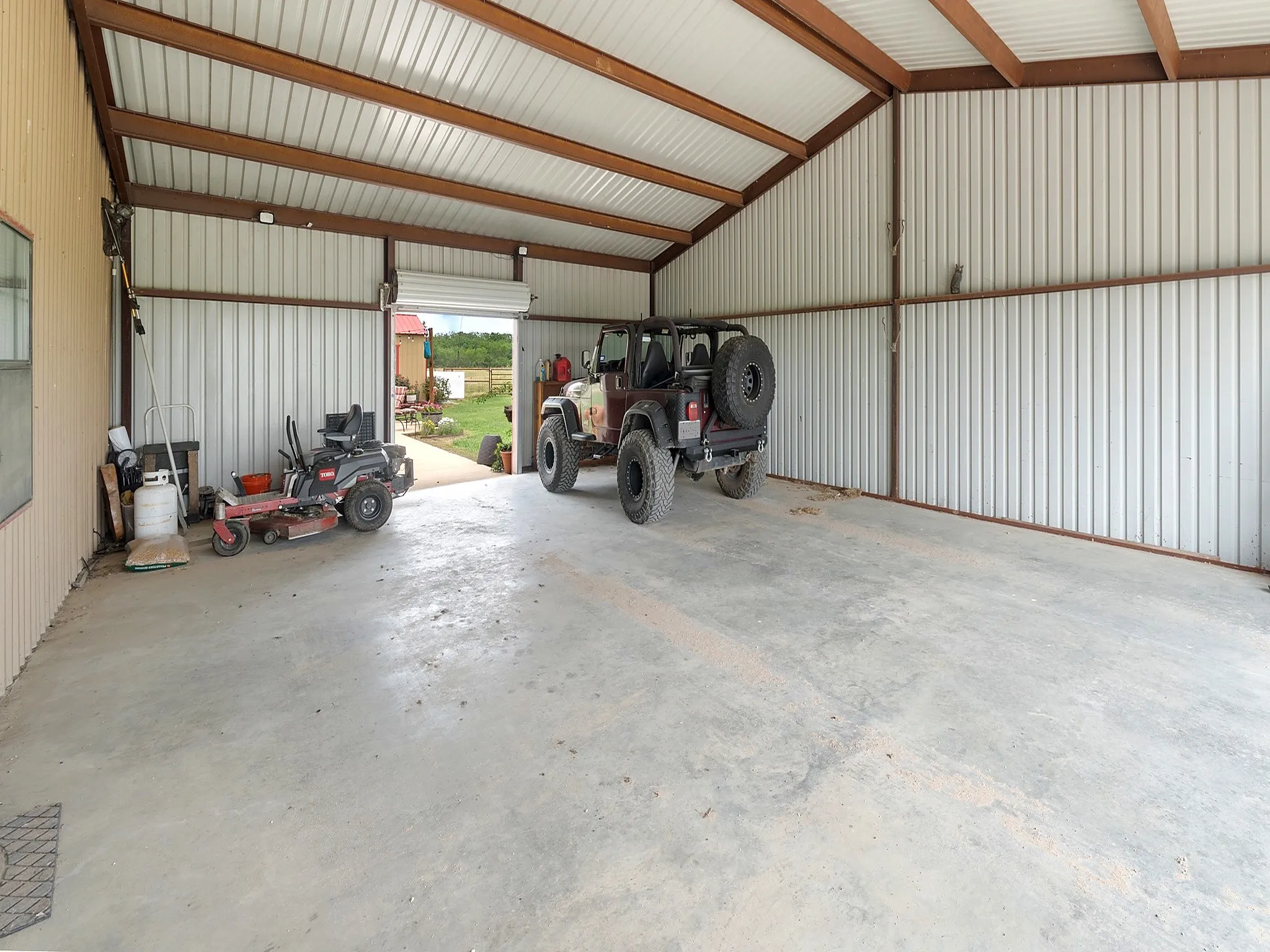 Detached metal-sided workshop featuring a concrete floor, exposed steel beams, vaulted ceiling, and an oversized roll-up garage door