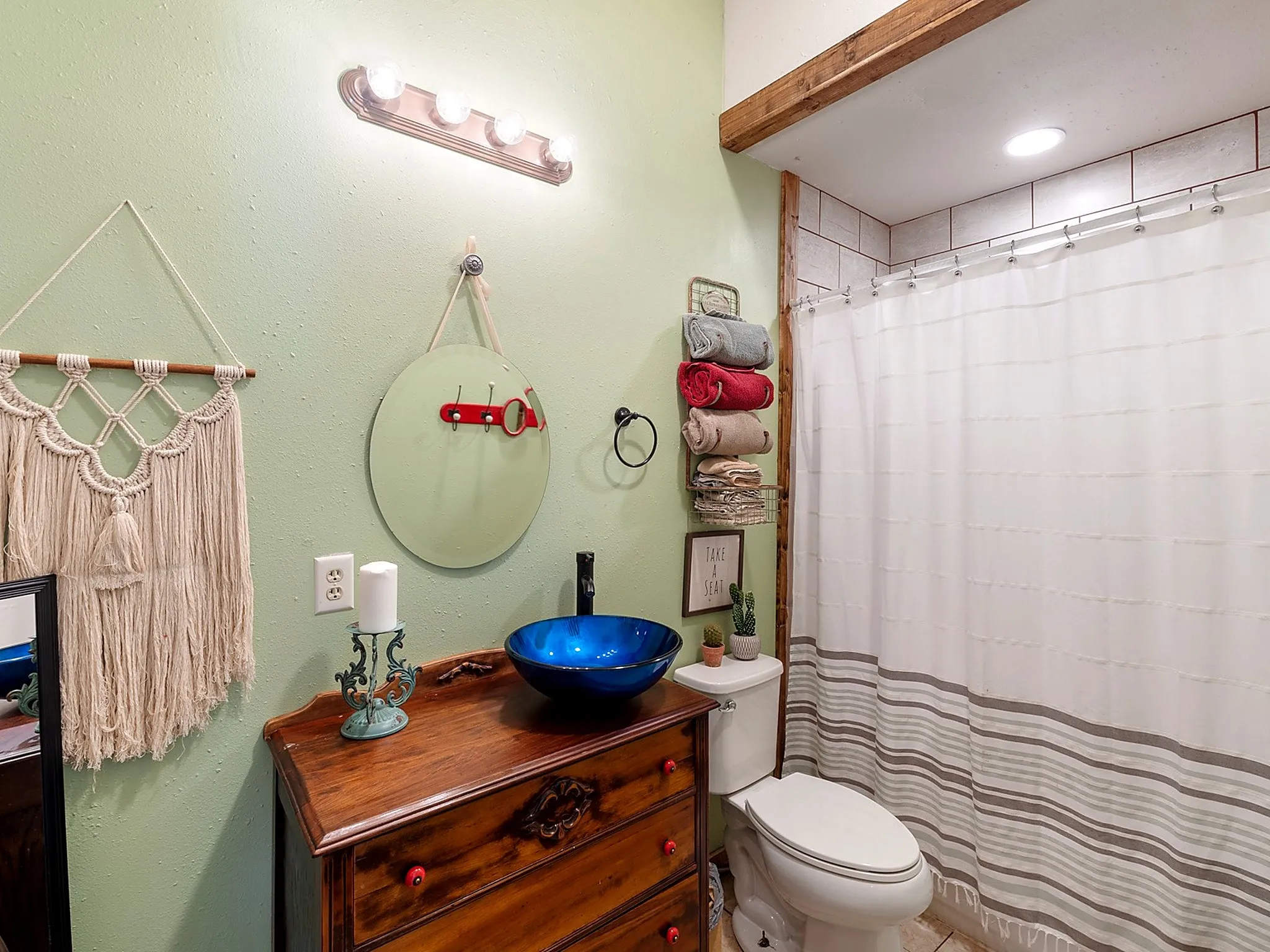 Bathroom vanity featuring a wooden base, blue glass vessel sink, matte black faucet, and a wall-mounted four-light fixture