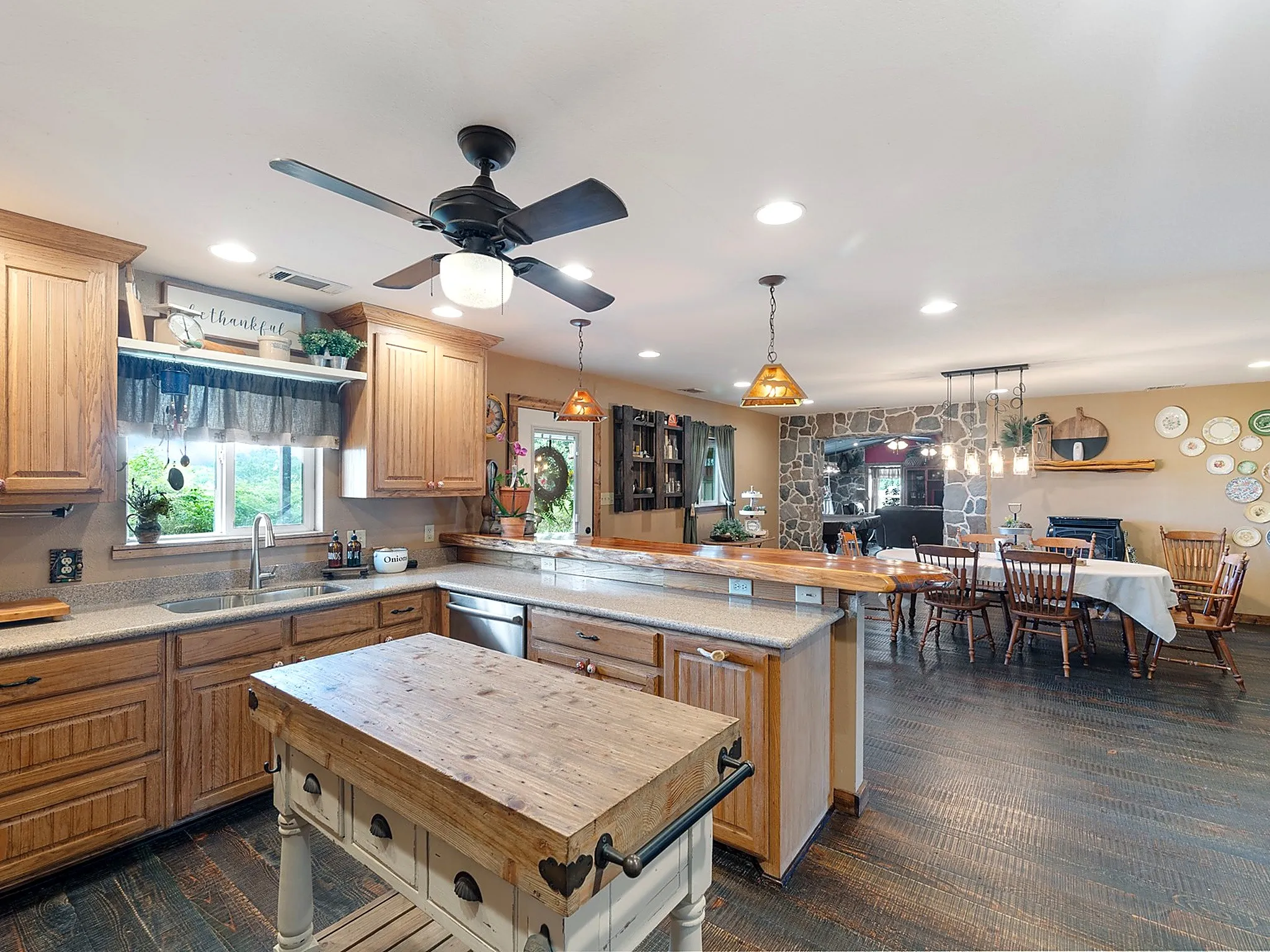 Kitchen featuring wood cabinetry, solid-surface countertops, a built-in breakfast bar with live-edge wood top, wood-finish flooring, and natural stone fireplace surround