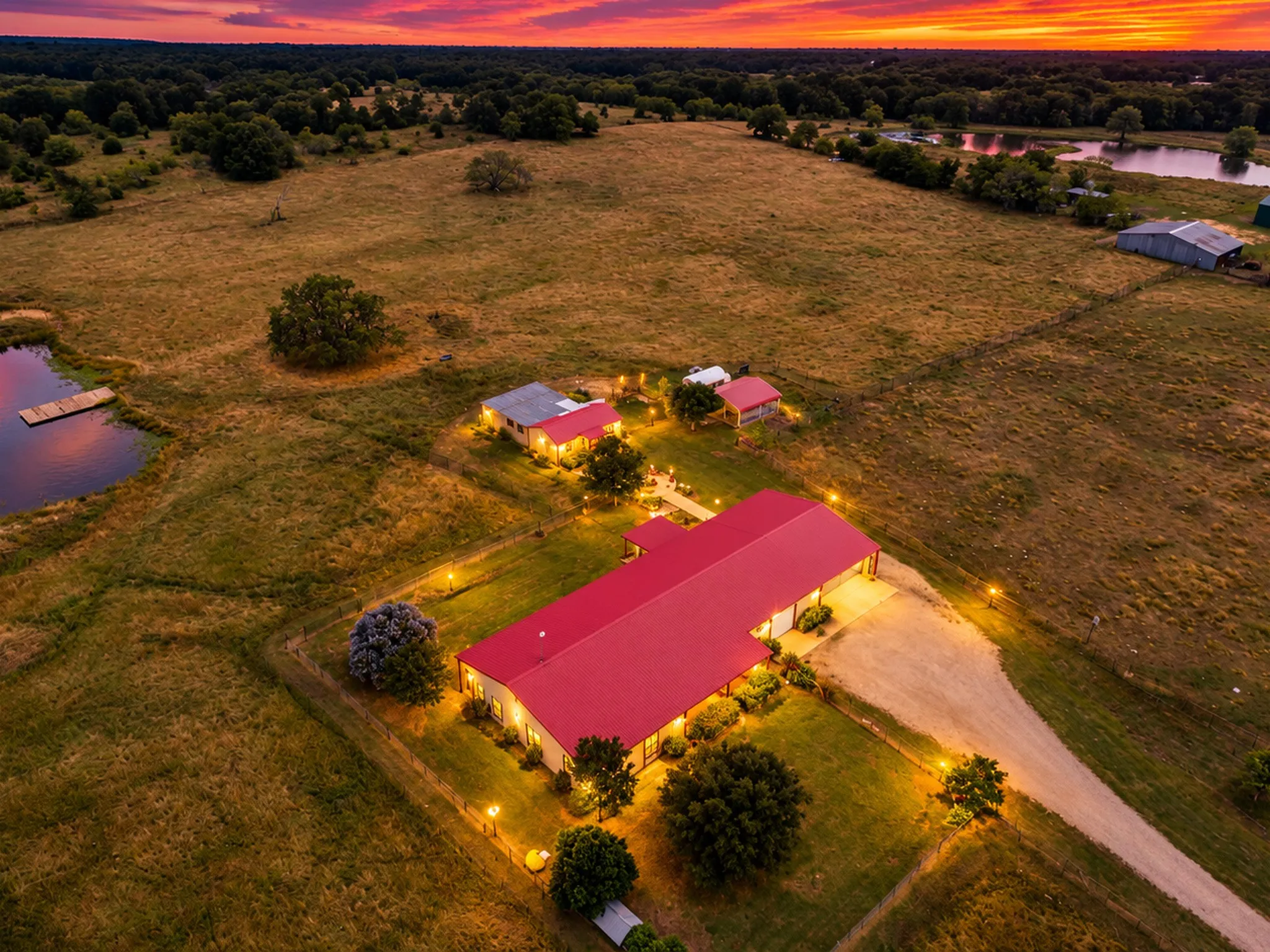 Expansive property featuring a red-roofed primary structure, multiple outbuildings, and a pond with a dock