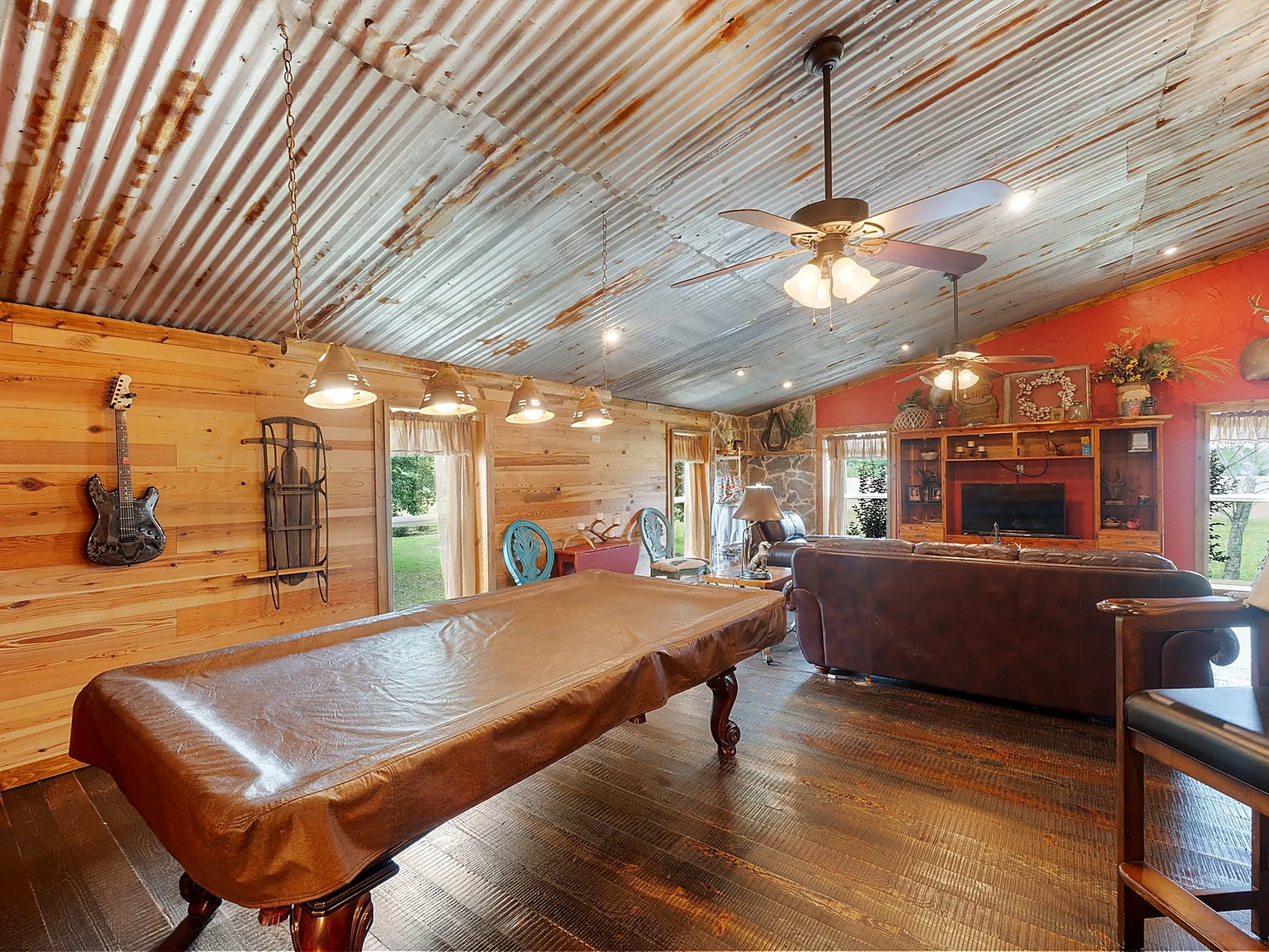 Corrugated metal ceiling, wood-finish flooring, accent wood plank wall, built-in entertainment center, and multiple ceiling fans