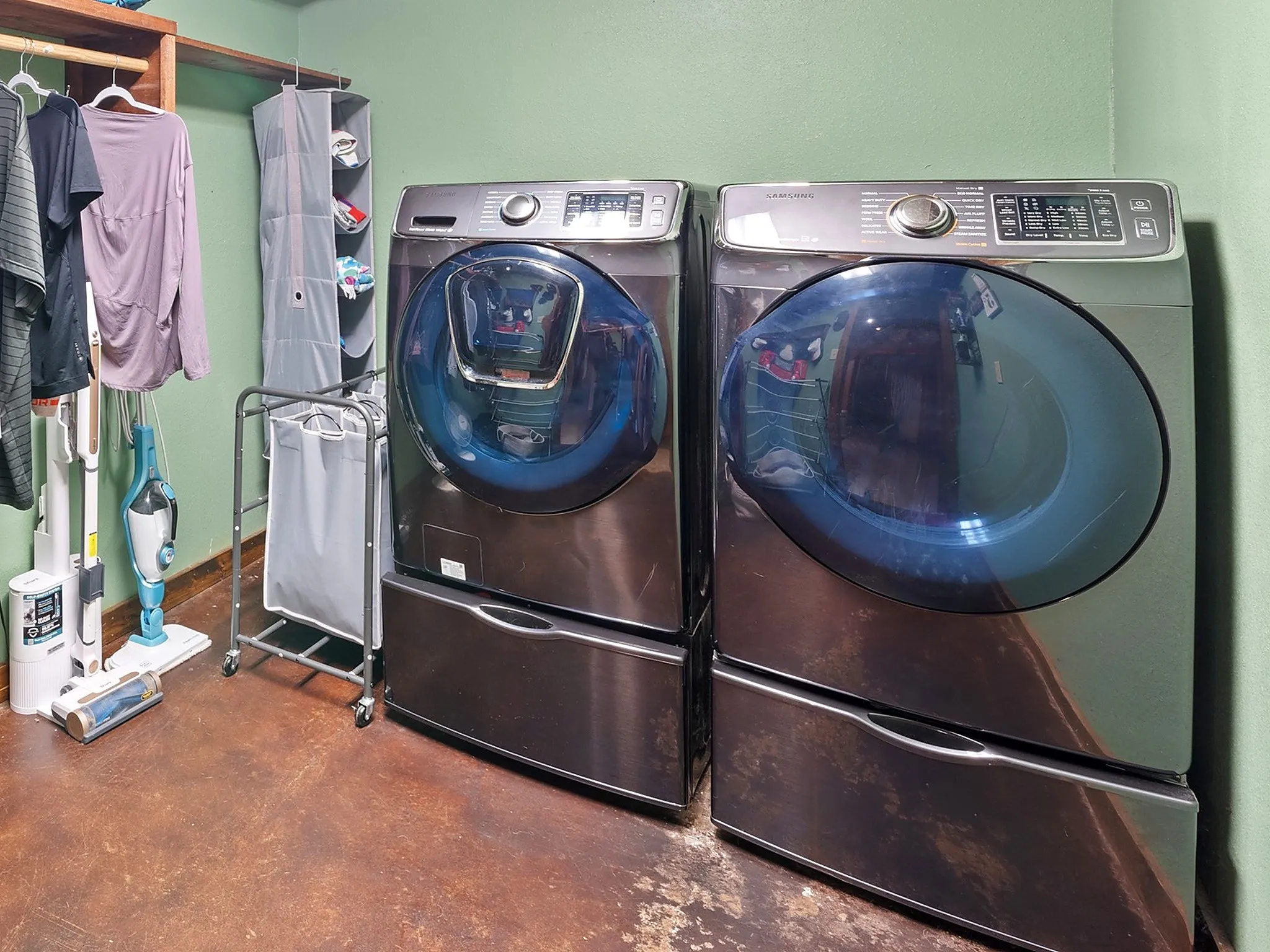 Laundry area featuring front-loading metallic finish washer and dryer with integrated storage pedestals and wall-mounted wooden shelving