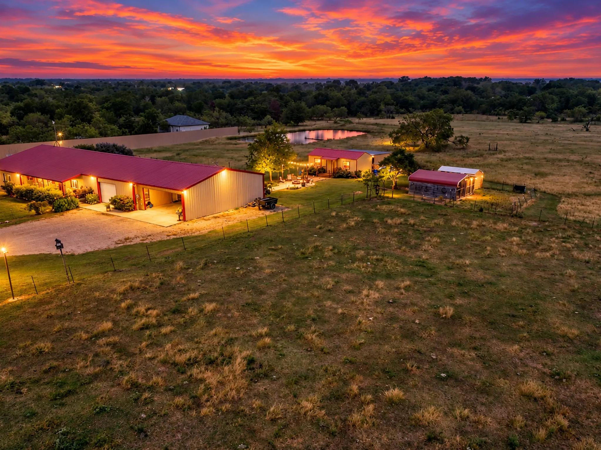 Expansive property featuring multiple structures with red metal roofing, a large pond, and mature landscaping