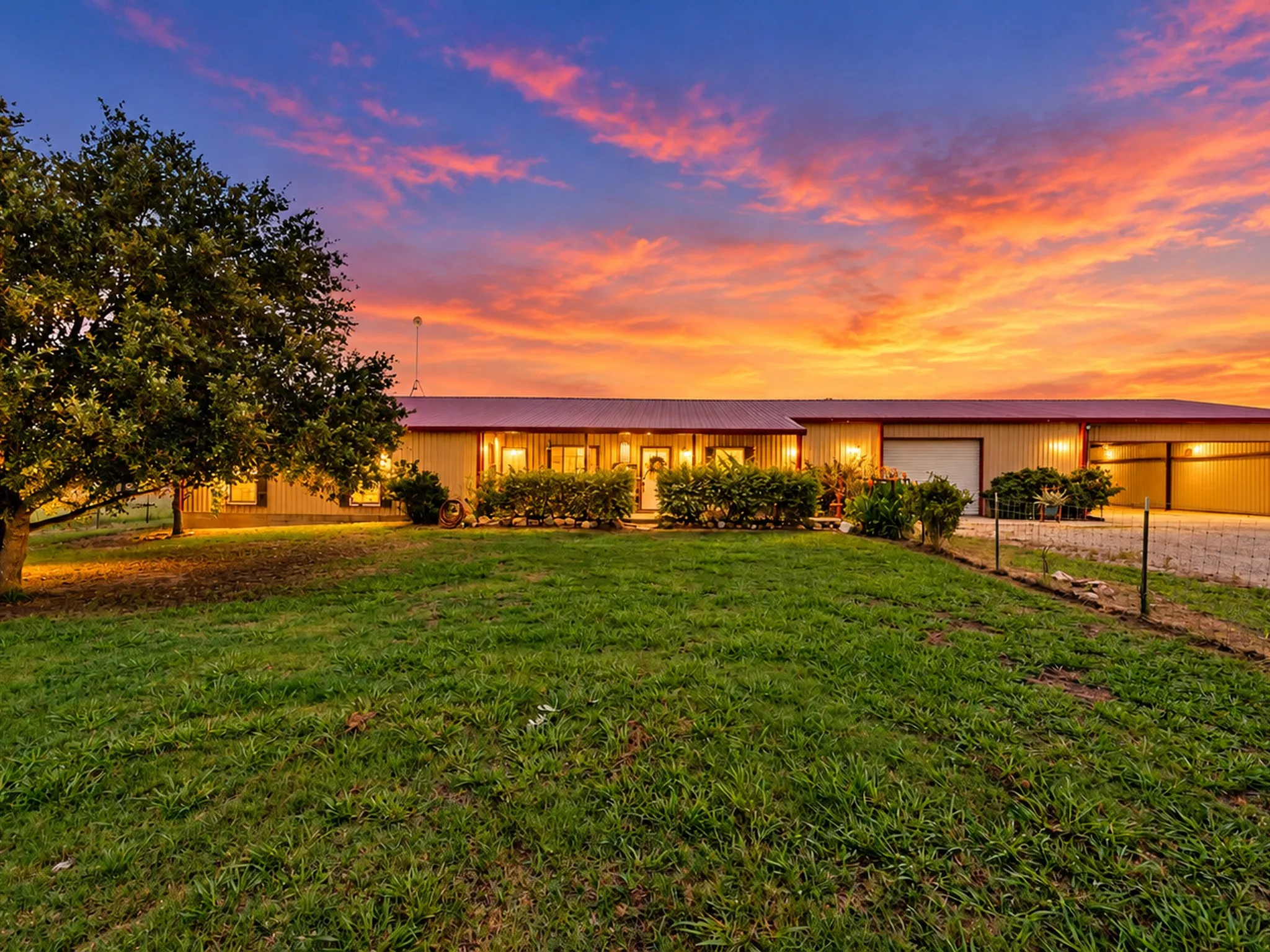 Expansive grassy area with mature trees, red metal roof, covered entry, and attached garage