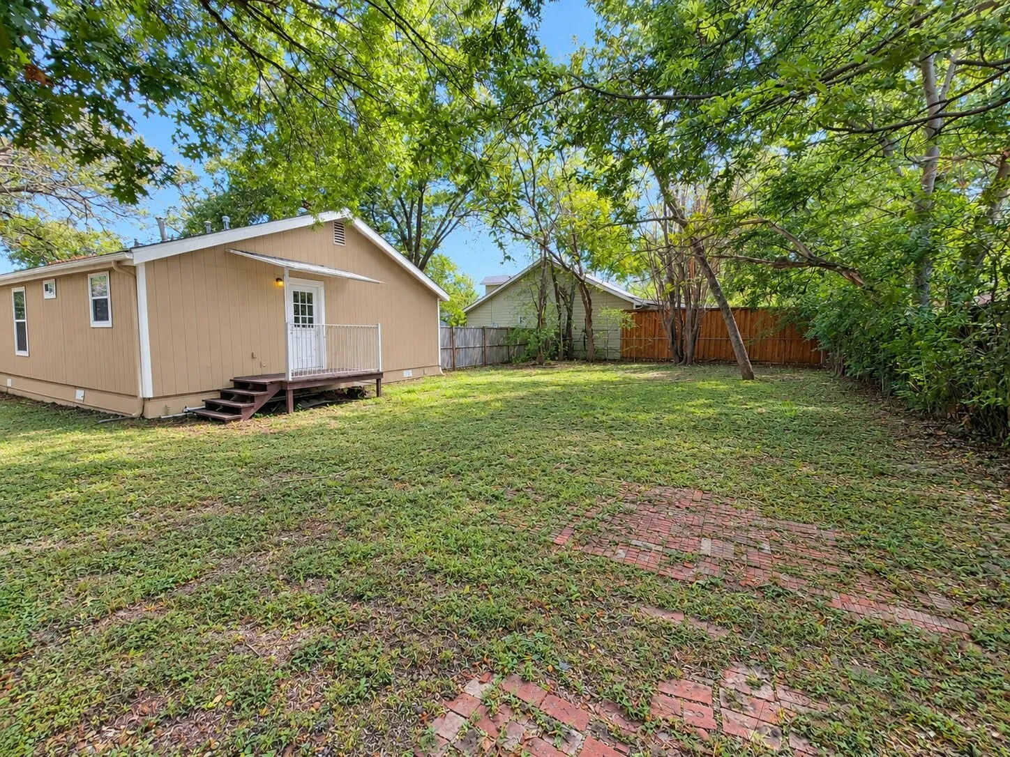 Expansive grassy yard with mature trees and a wood privacy fence