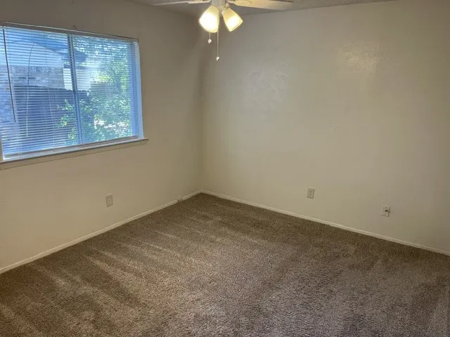 Neutral-toned wall-to-wall carpeting, single-pane horizontal sliding window, and ceiling-mounted light fixture with a central fan