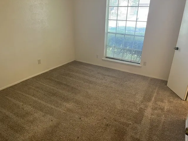 Neutral-toned wall-to-wall carpeting, single-pane window with a grid pattern, and solid-core interior door