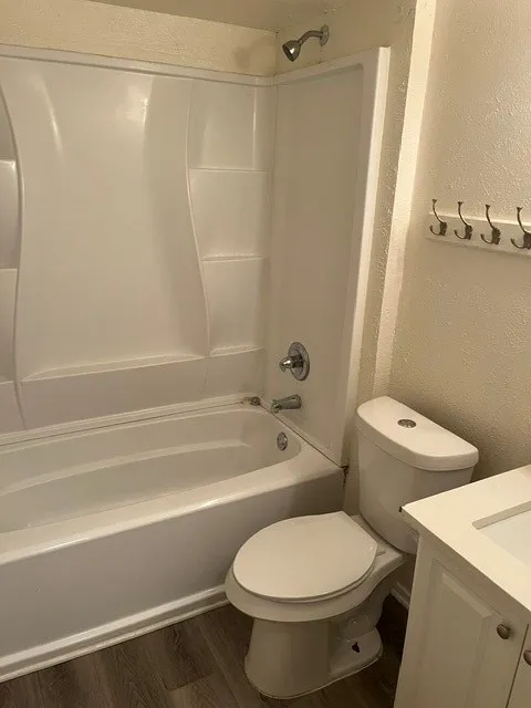 Bathroom featuring a white molded tub-and-shower surround, wood-finish flooring, a wall-mounted hook rack, and a vanity cabinet