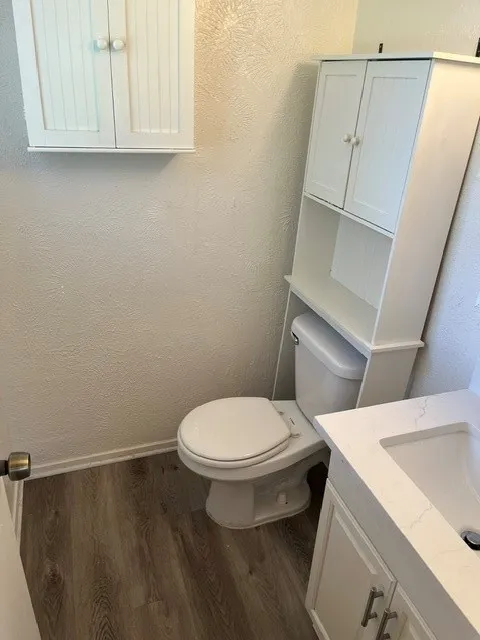Bathroom featuring wood-finish flooring, white cabinetry with beadboard detailing, an over-the-toilet storage unit, and a vanity with a white countertop and rectangular undermount sink