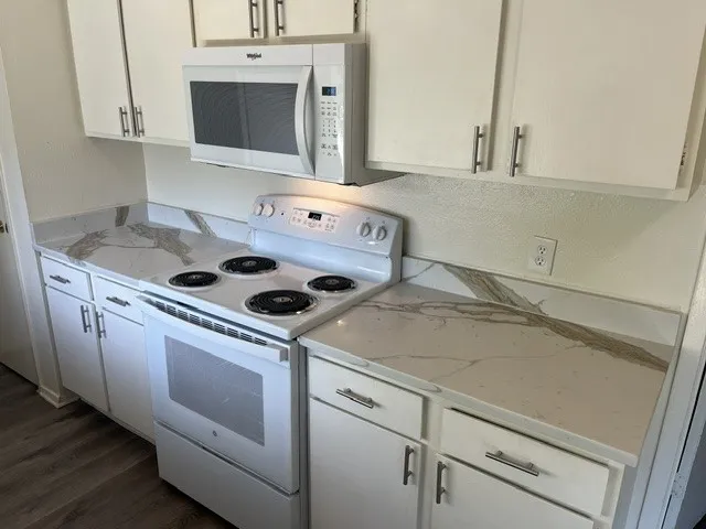 White cabinetry with brushed nickel hardware, stone-patterned countertops, integrated backsplashes, a white electric range, and an over-the-range microwave