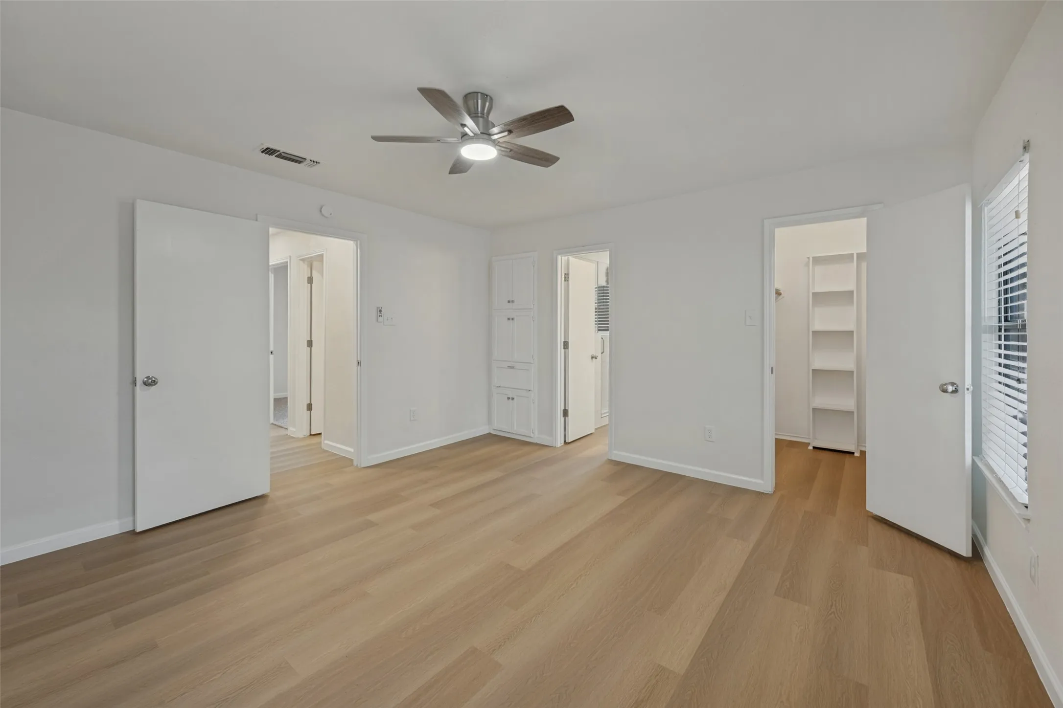 Bathroom featuring a wood-finish floor, a vanity with a white countertop and rectangular sink, a wall-mounted rectangular mirror, and a tub-shower combination with light-toned stone-finish tile surround and a built-in recessed niche