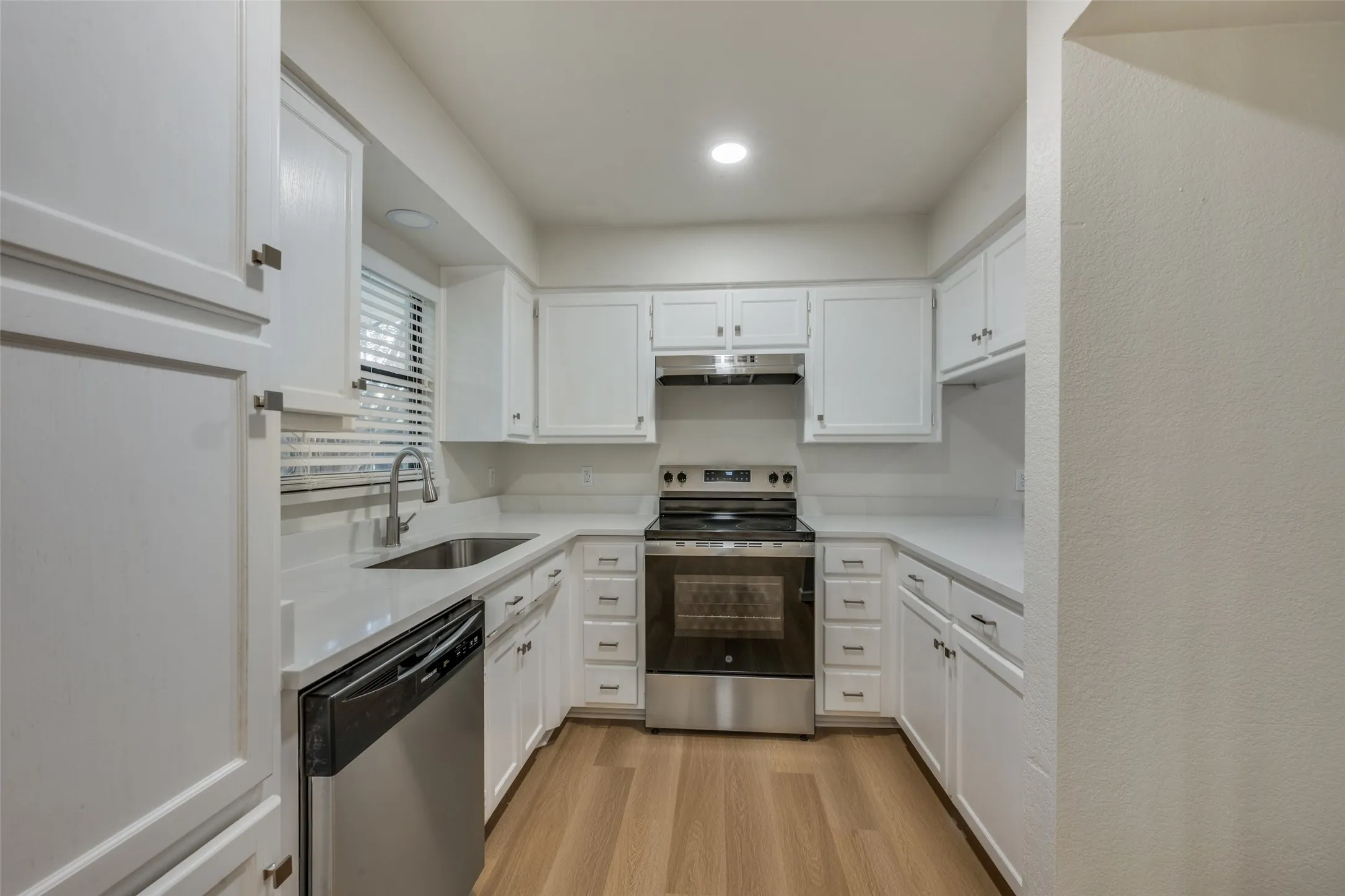 Kitchen featuring white cabinetry, solid-surface countertops, stainless steel appliances, and wood- flooring