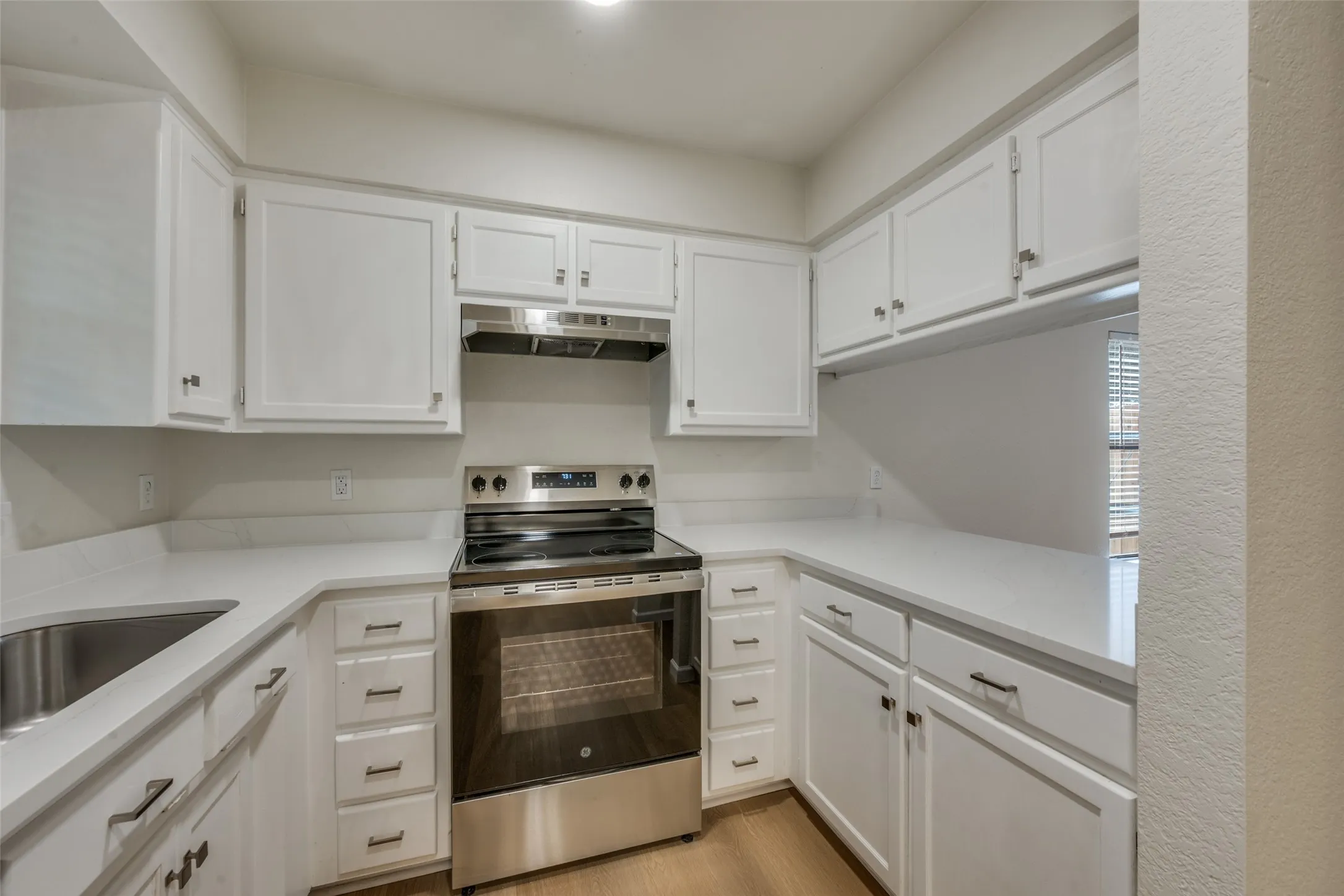 Kitchen featuring white cabinetry, solid-surface countertops, stainless steel electric range, undermount stainless steel sink, and wood-finish flooring