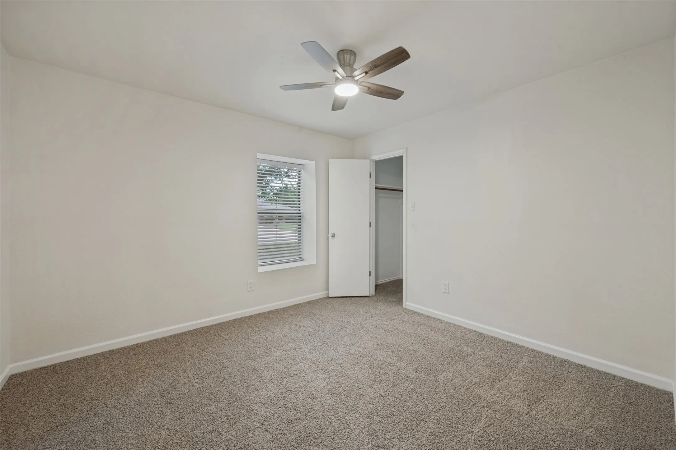 Neutral interior space featuring neutral wall tones, textured carpeting, a multi-blade ceiling fan with integrated lighting, and a walk-in closet with built-in shelving