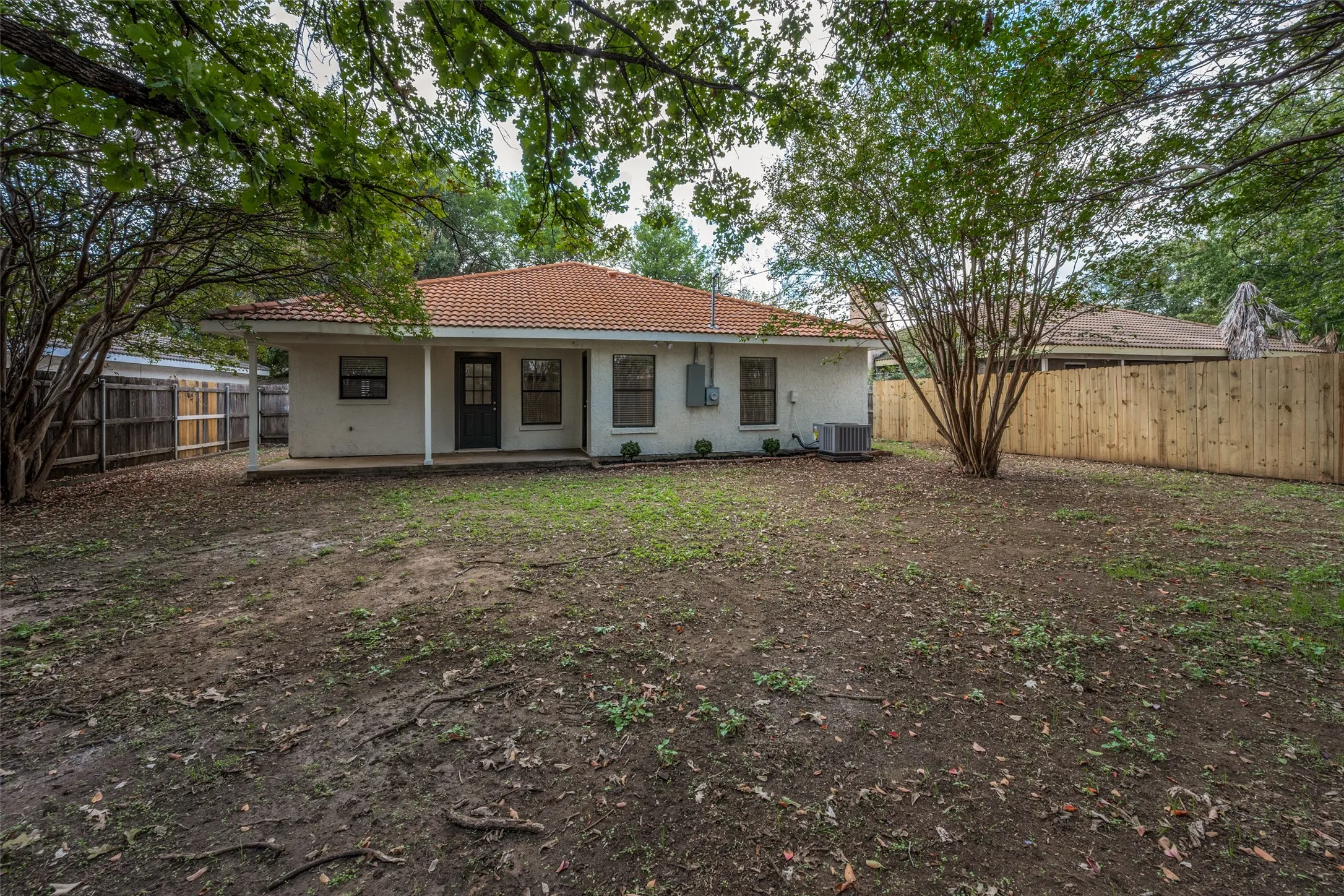 Rear exterior featuring a tile roof, covered porch, and wood privacy fencing