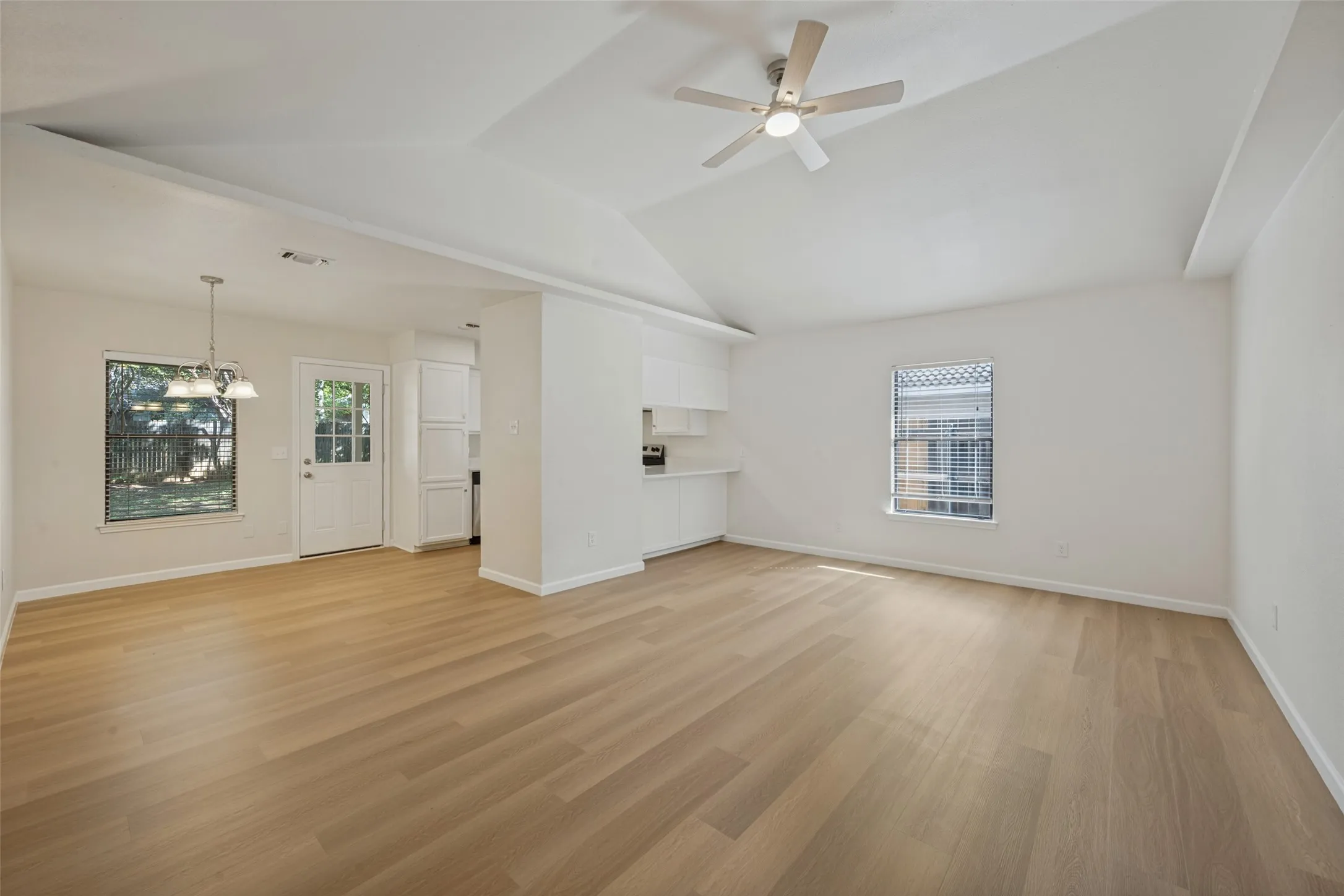 Vaulted ceilings featuring a central overhead fan, wood-finish flooring, and natural lighting provided by multi-pane windows