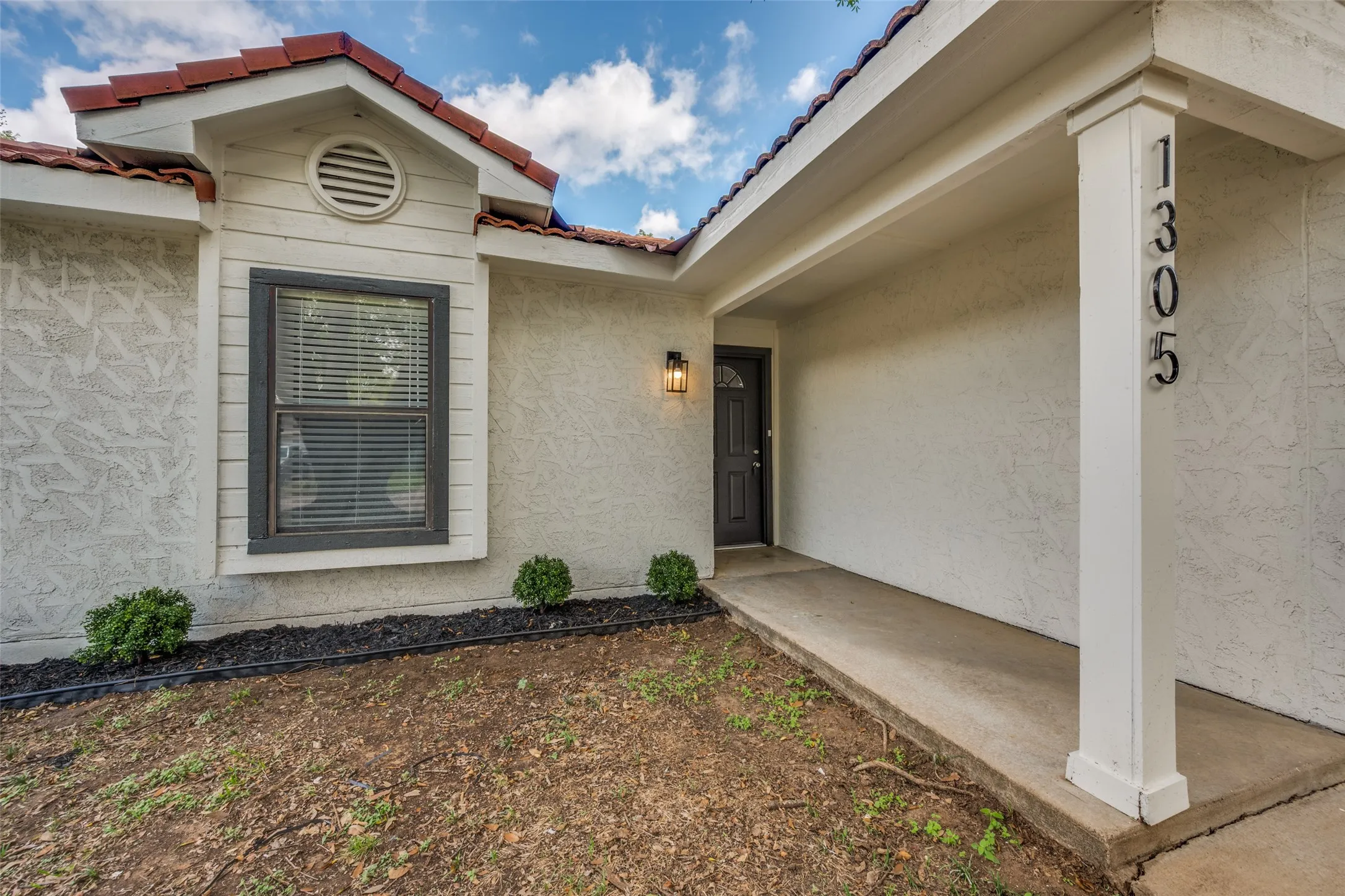 Stucco exterior featuring a covered entryway, tile roof, and a single-hung window with dark trim