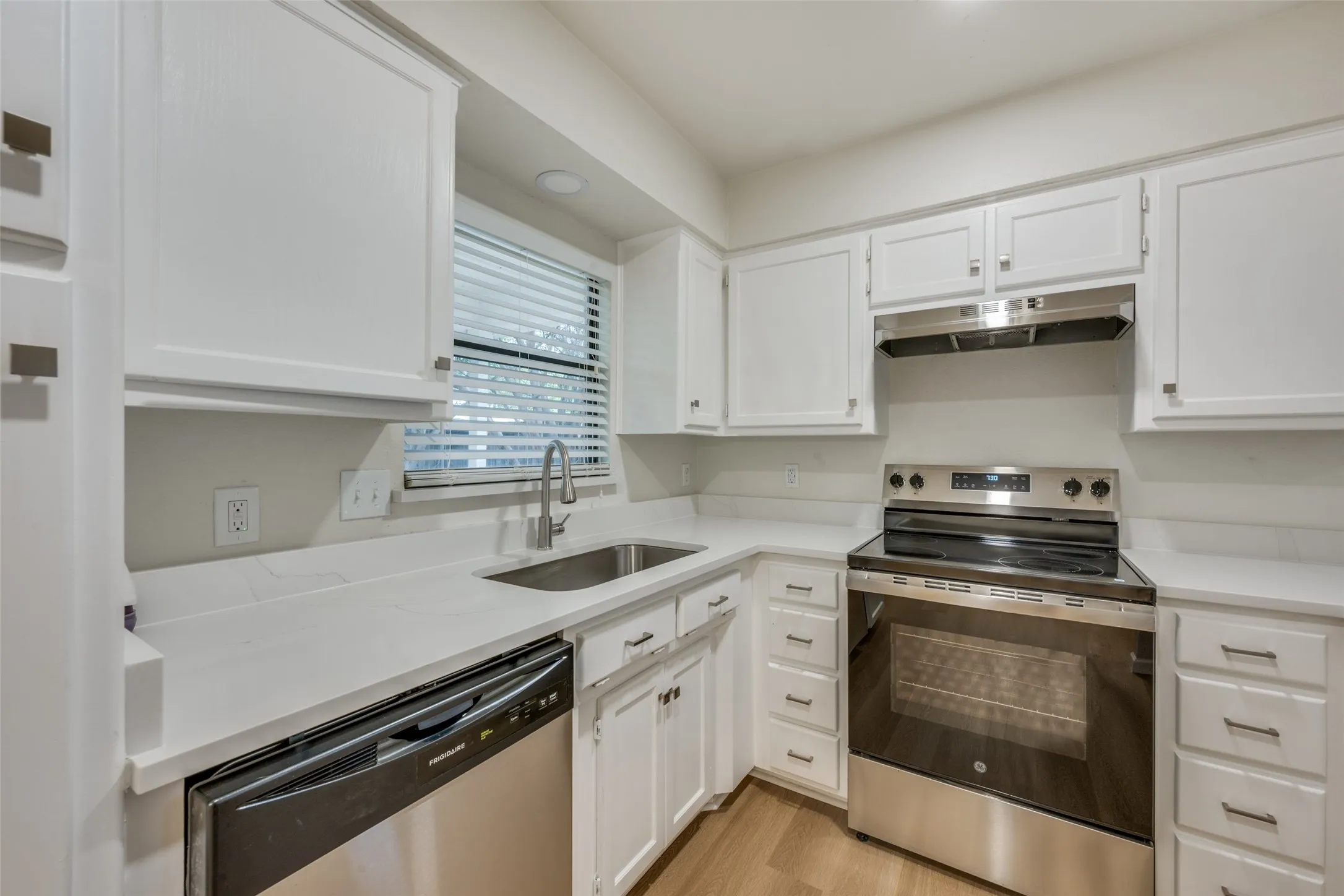 Kitchen featuring white cabinetry, solid-surface countertops, stainless steel appliances, an undermount sink with a gooseneck faucet, and wood-finish flooring