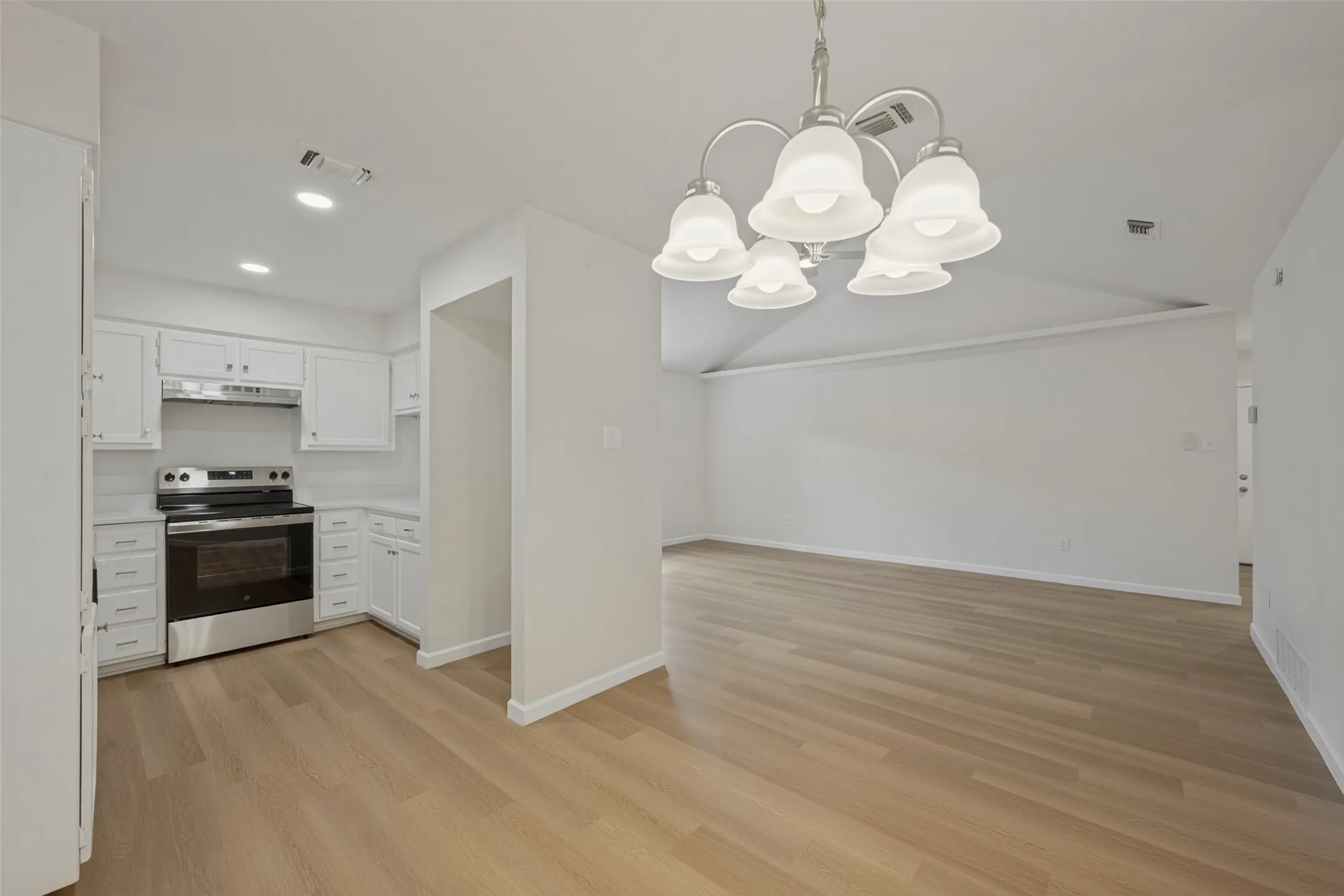 Kitchen featuring white cabinetry, stainless steel range, and wood-finish flooring, complemented by a multi-light chandelier and vaulted ceiling