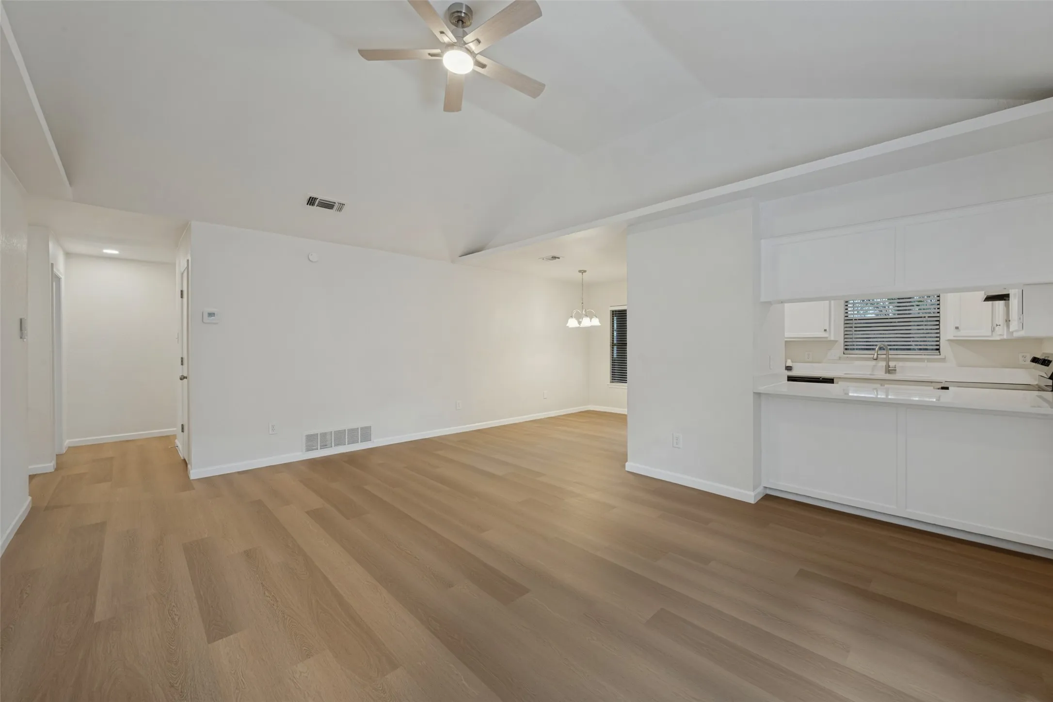 Vaulted ceilings, wood-finish flooring, recessed lighting, ceiling fan with integrated light, and white cabinetry