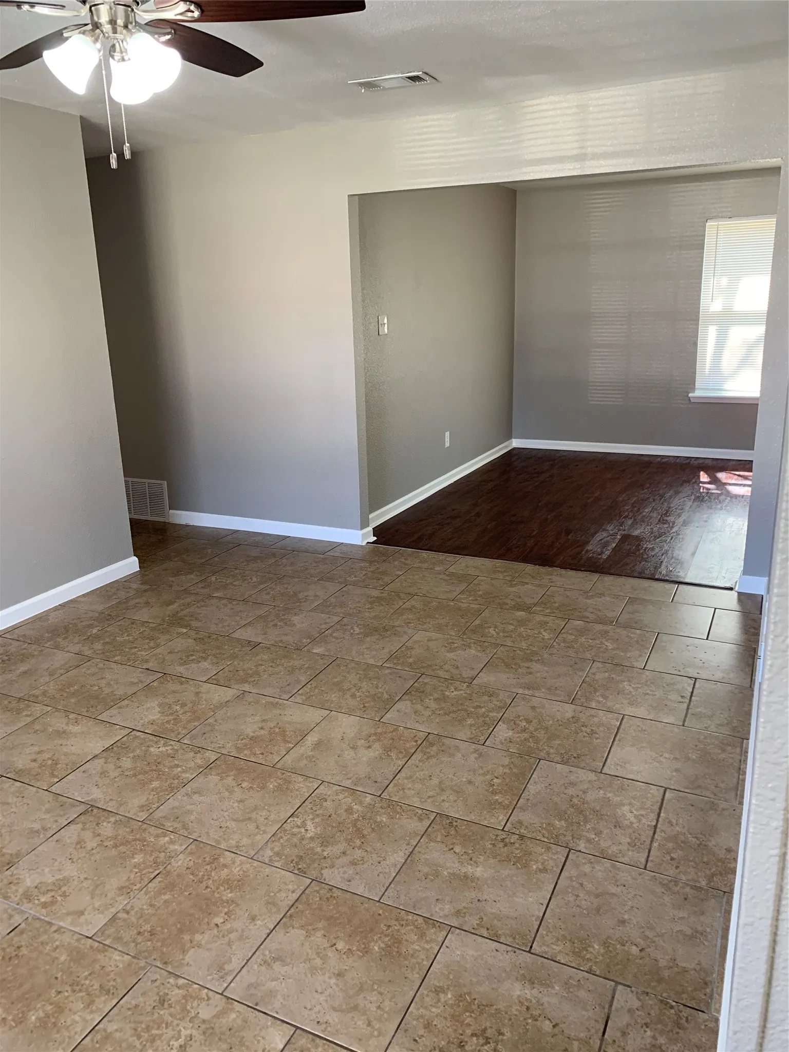 Interior space featuring large-format ceramic tile flooring, dark wood-finish flooring, and a ceiling-mounted light fixture with a fan