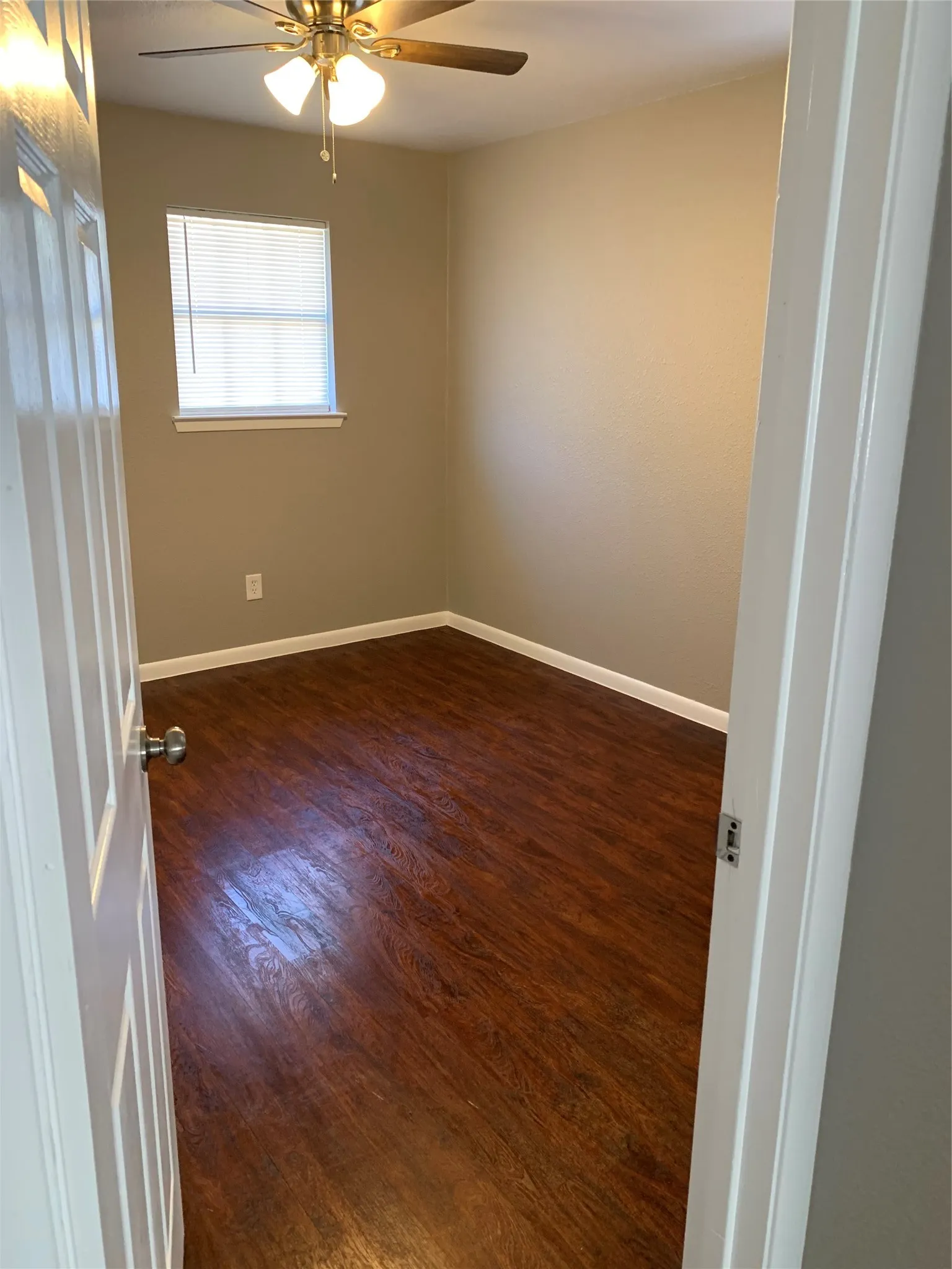 Interior space featuring dark wood-finish flooring, neutral wall paint, a ceiling fan with integrated lighting, and a single-pane window