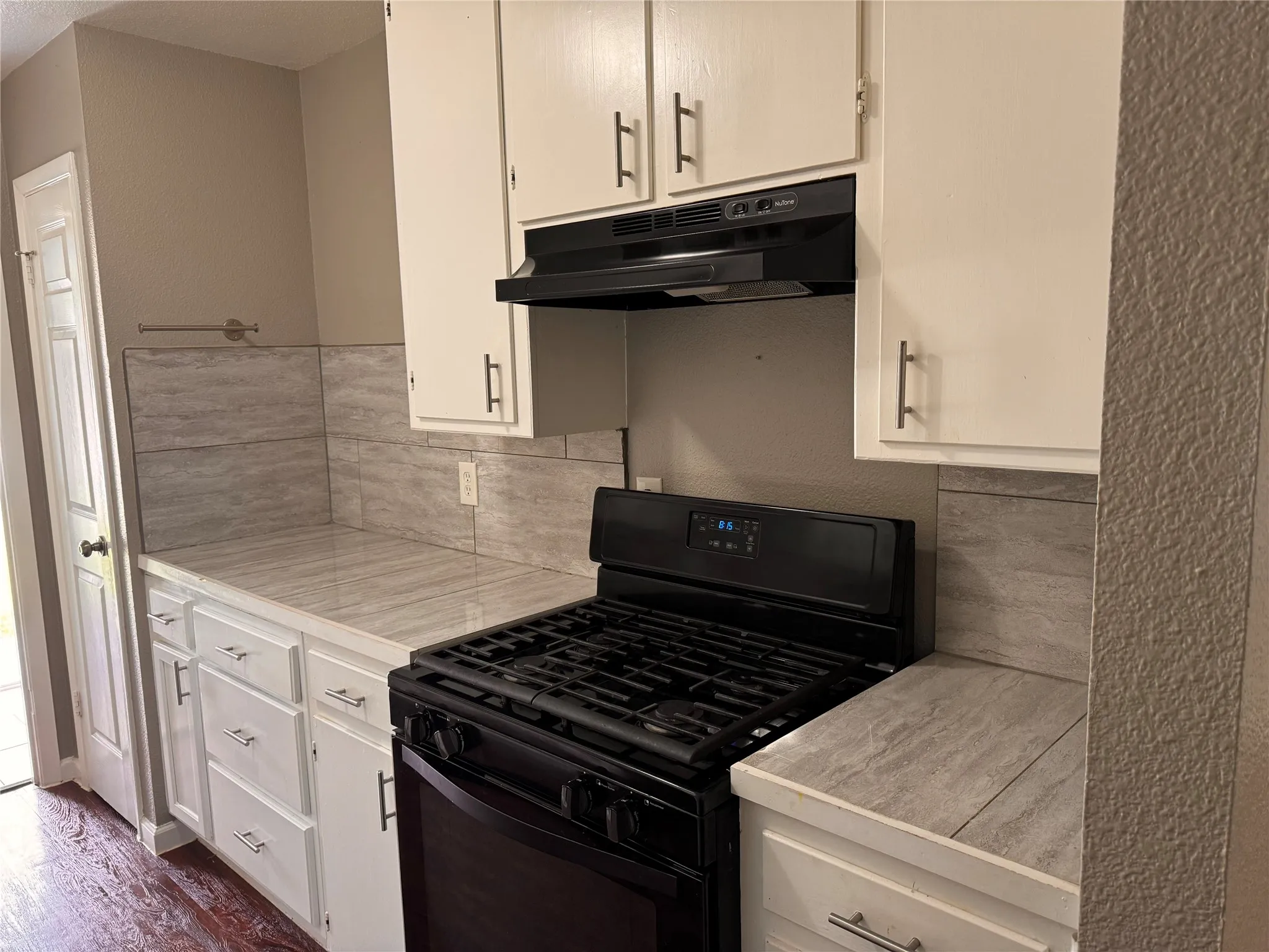 Kitchen featuring white cabinetry with brushed metal pulls, stone-finish countertops, tile backsplash, and a black built-in range with a matching range hood