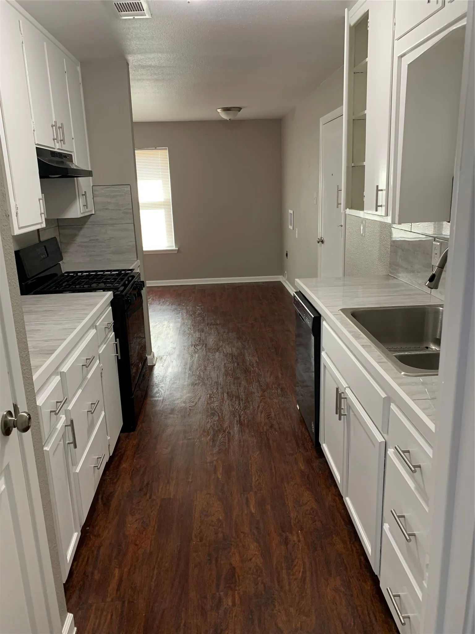 Kitchen featuring white shaker-style cabinetry, wood-finish flooring, light-toned countertops, tile backsplash, and dark-finish appliances