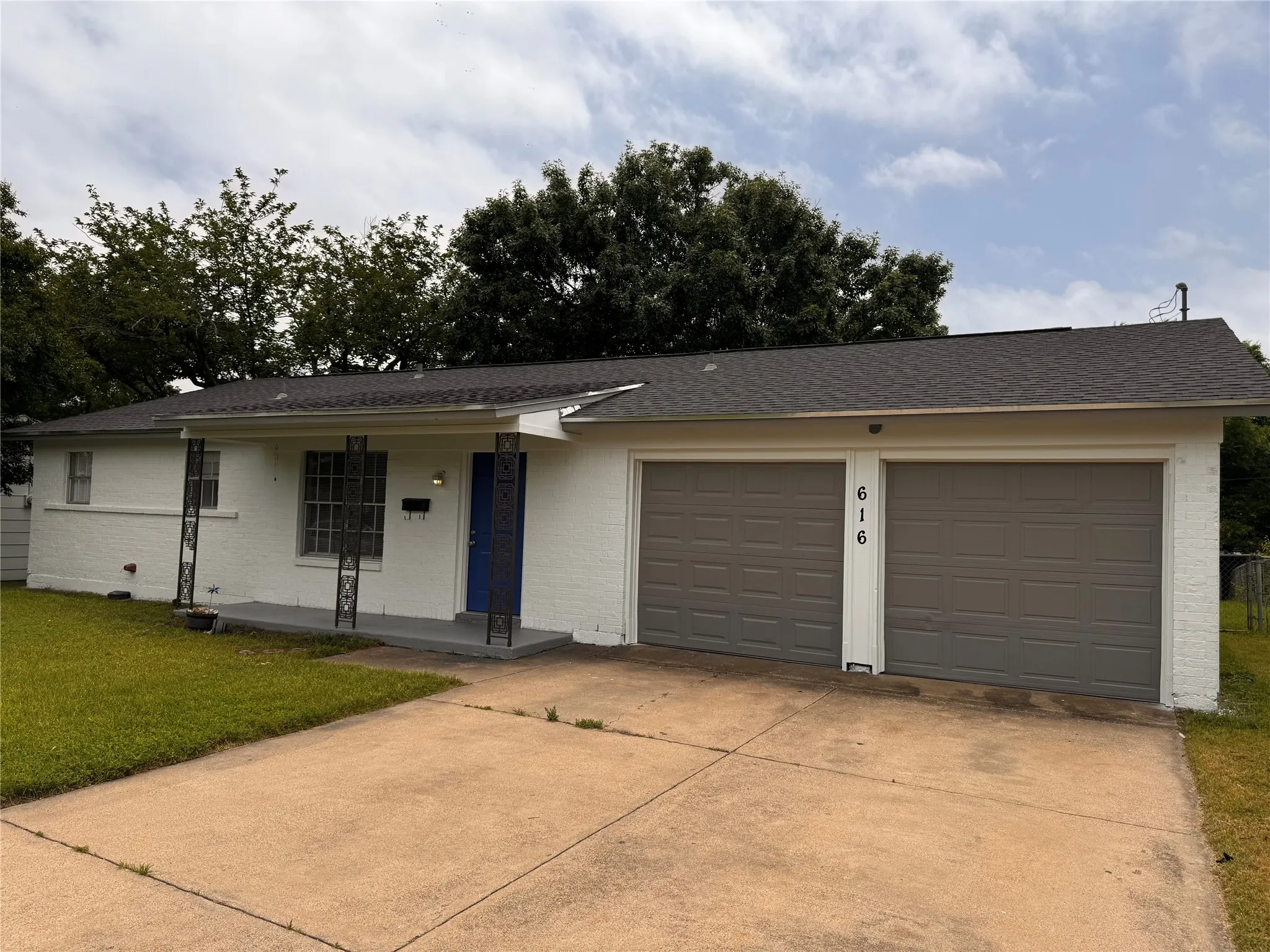 Painted brick exterior featuring a covered front porch with decorative iron columns and an attached two-car garage