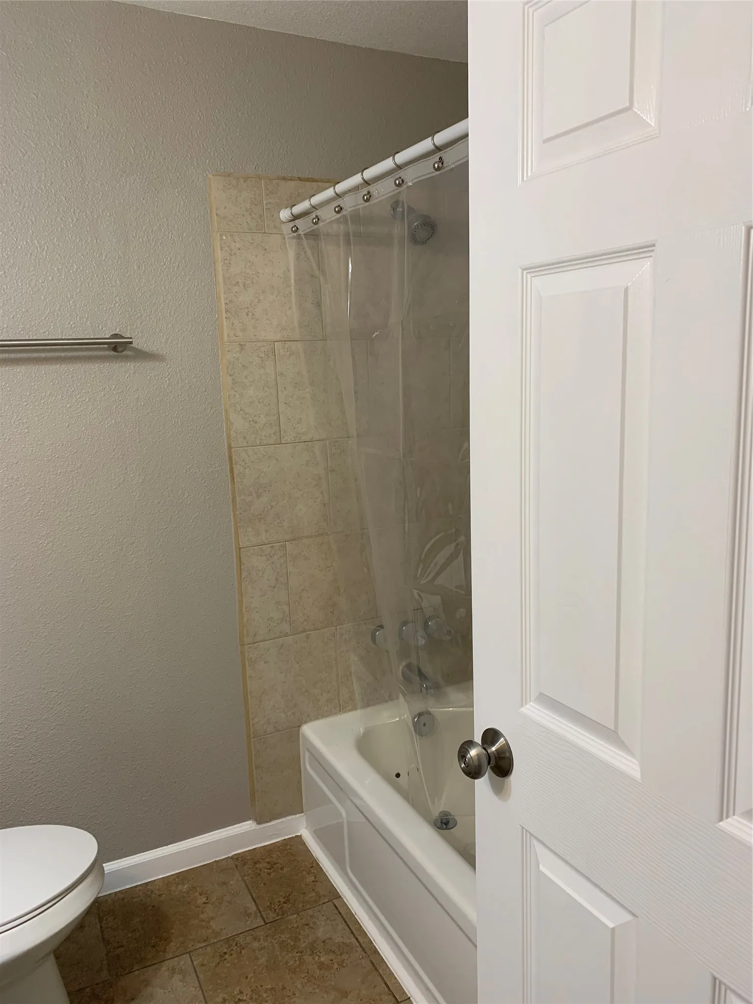 Bathroom featuring a tub with stone-finish tile surround, a stainless steel shower fixture, a metal towel bar, and large-format floor tiles