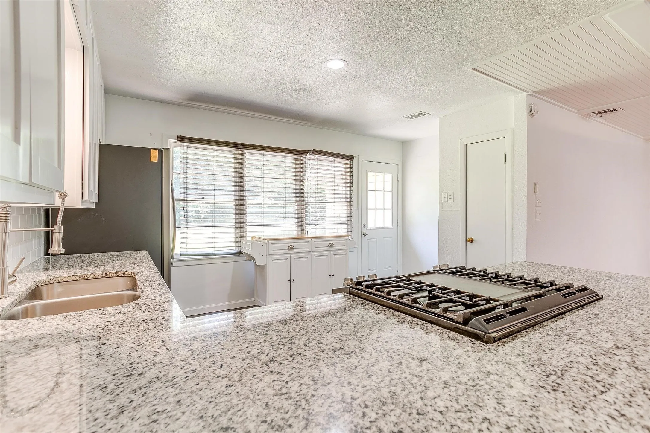 Kitchen featuring a healthy amount of sunlight, light stone counters, and white cabinetry