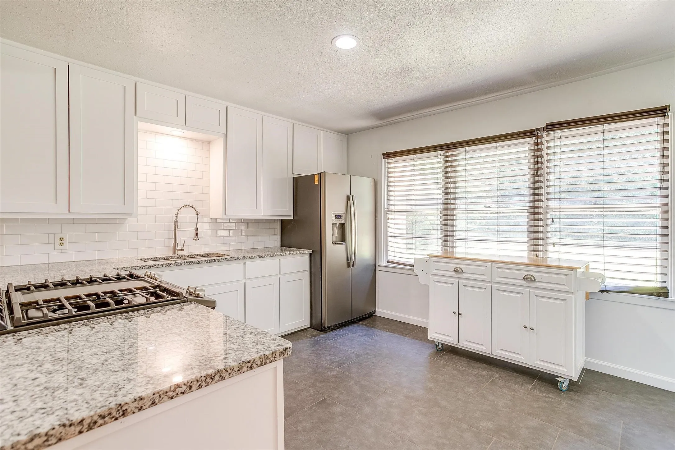 Kitchen with white cabinetry, stainless steel fridge, tile floors, backsplash, and sink