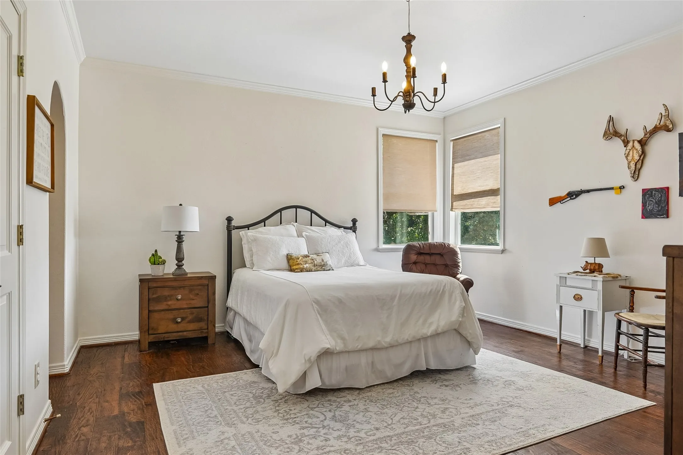 Spacious room featuring wood-finish flooring, crown molding, double-hung windows, and a multi-arm chandelier